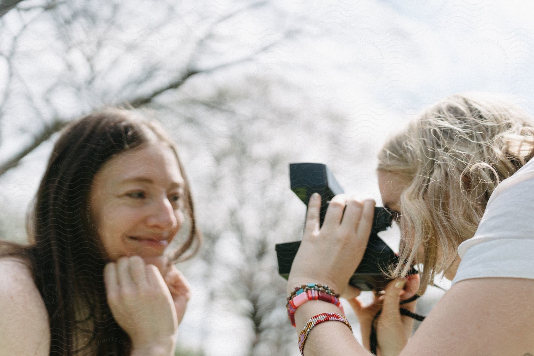 Two teenage girls are outside as one girl holds a camera taking a picture of her friend