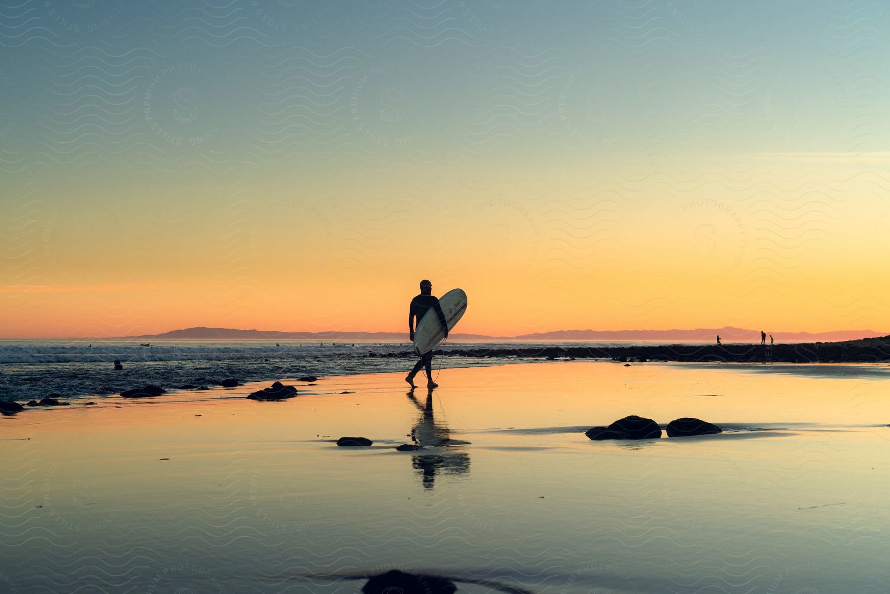 Man carries his surfboard as he walks across the beach