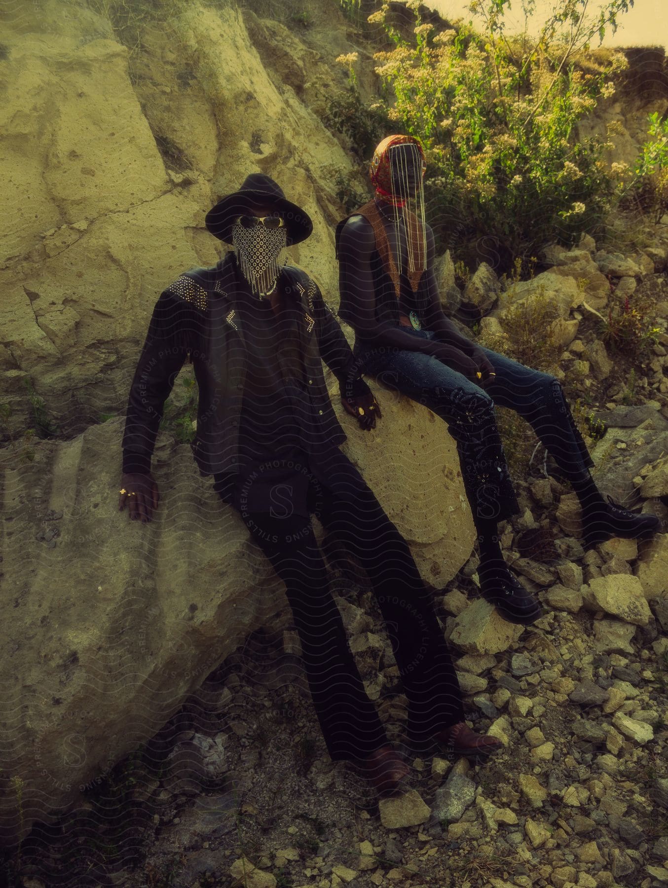 Two people wearing masks to cover their faces, sitting on a rock formation.