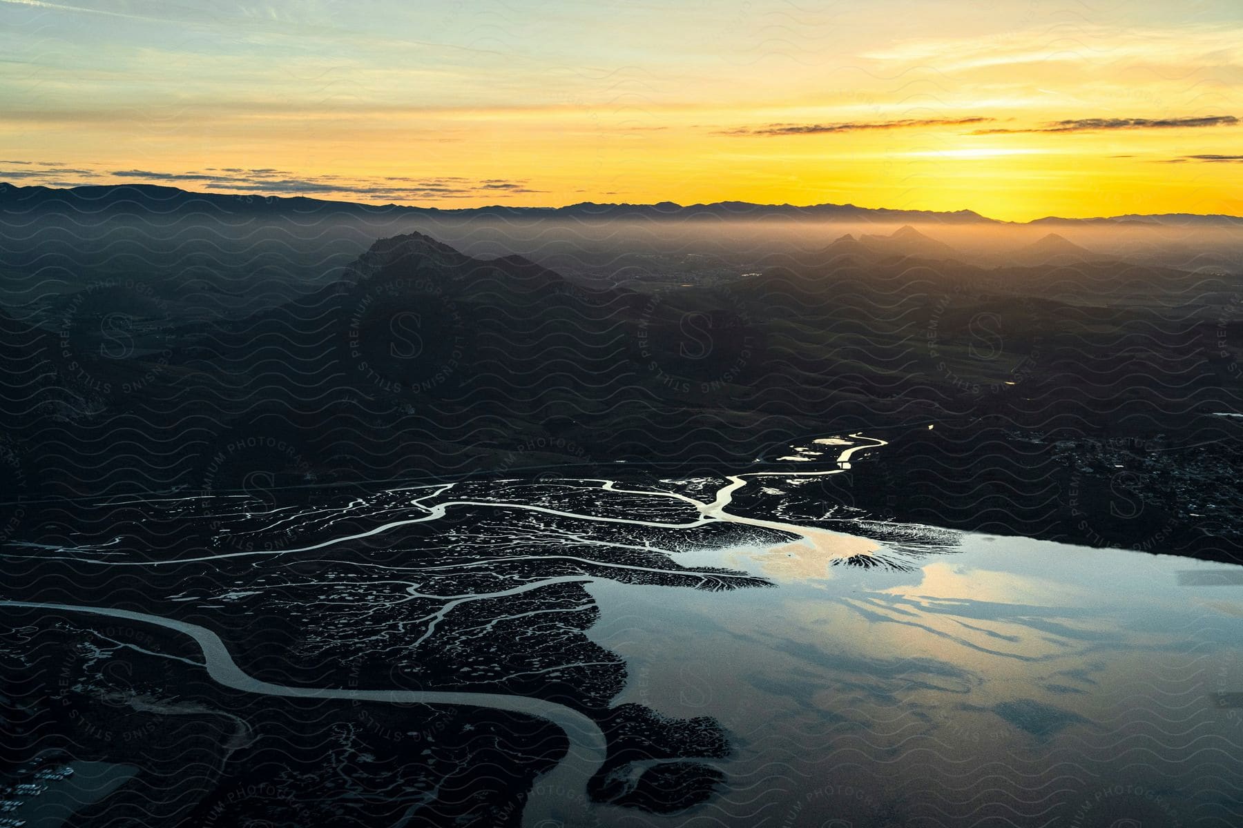 An aerial view of a winding river through a mountainous landscape at sunset.