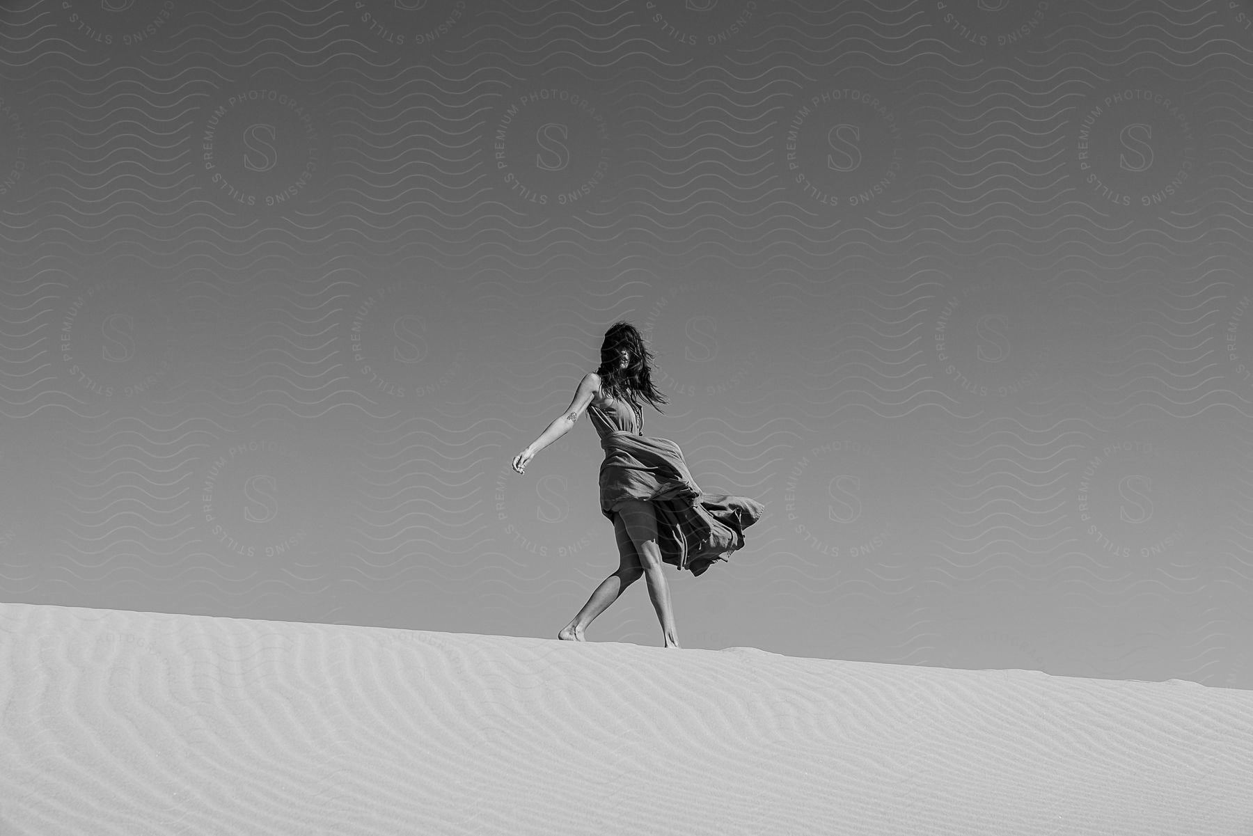 A woman walks along the crest of a sand dune.