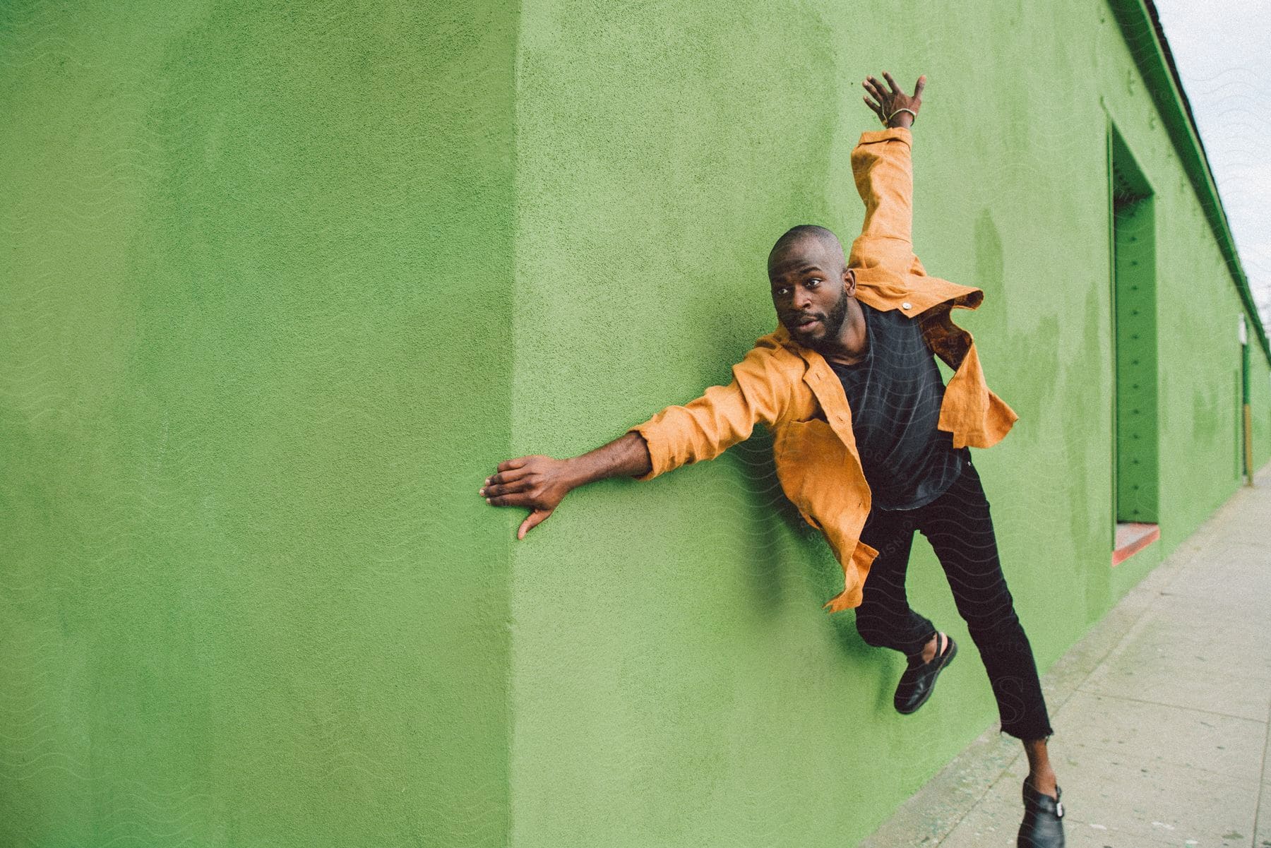 A man in a yellow coat is holding onto the green wall as if he is running