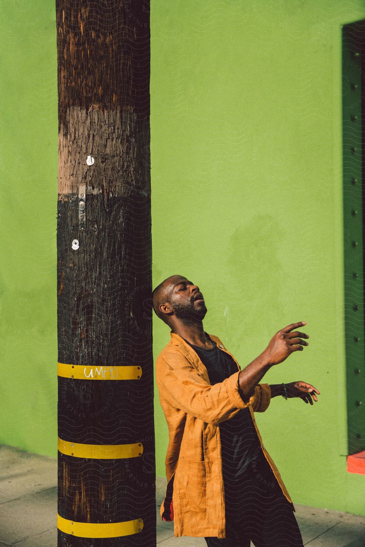 Stock photo of a man in a yellow jacket leans against a wooden pole with a vibrant green background