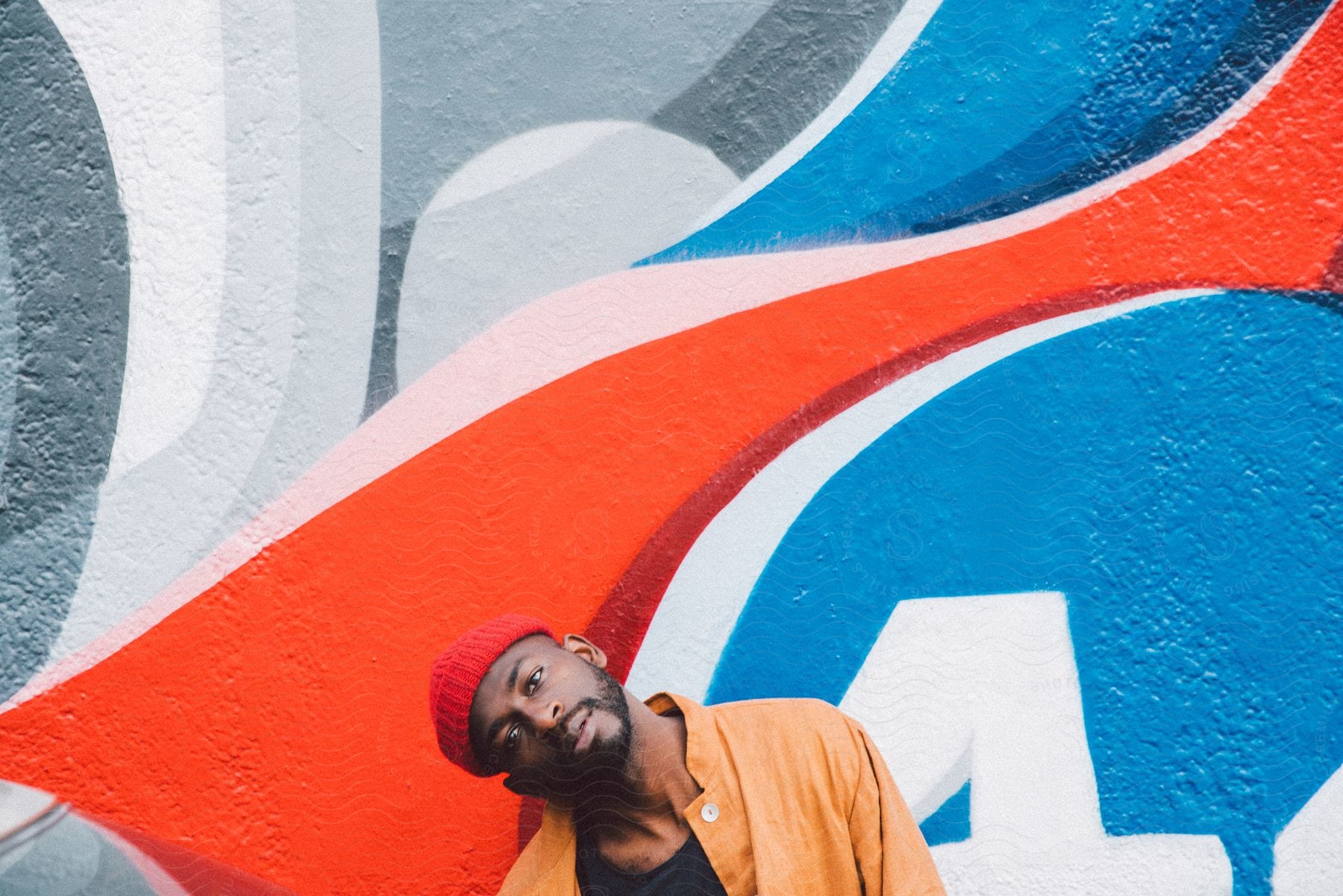 Man with red cap leaning against a wall with colorful graffiti