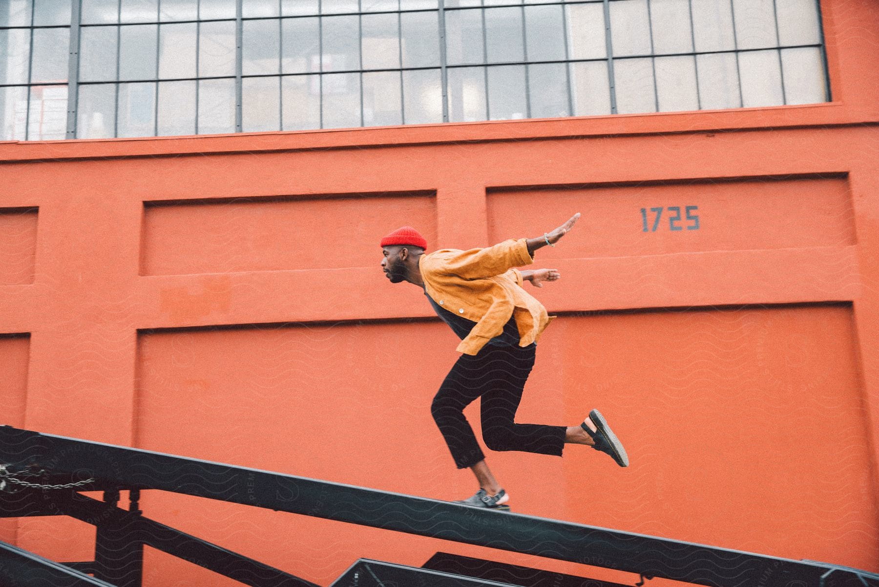 Stock photo of man running with his arms behind him on a metal surface against a vibrant orange wall.