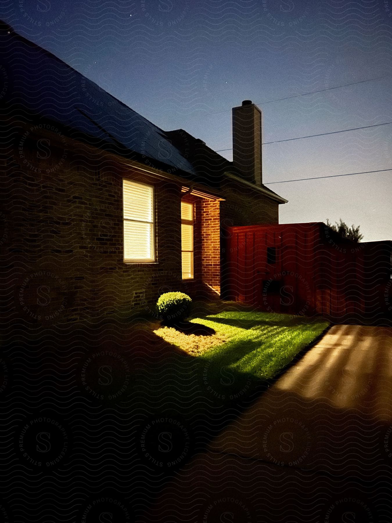 a brick house whose interior lighting shines onto the yard outside.