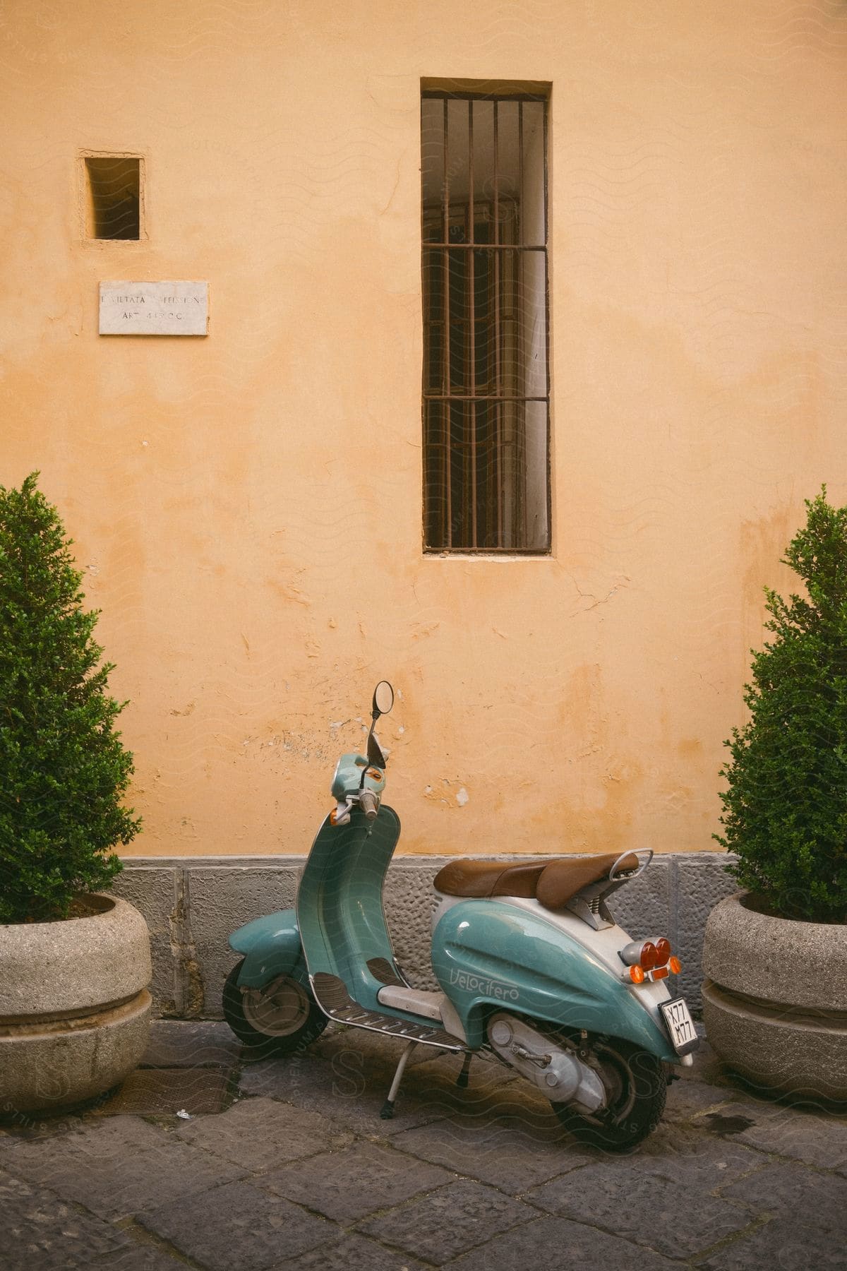 A light blue motor scooter is parked outside a light orange concrete building.
