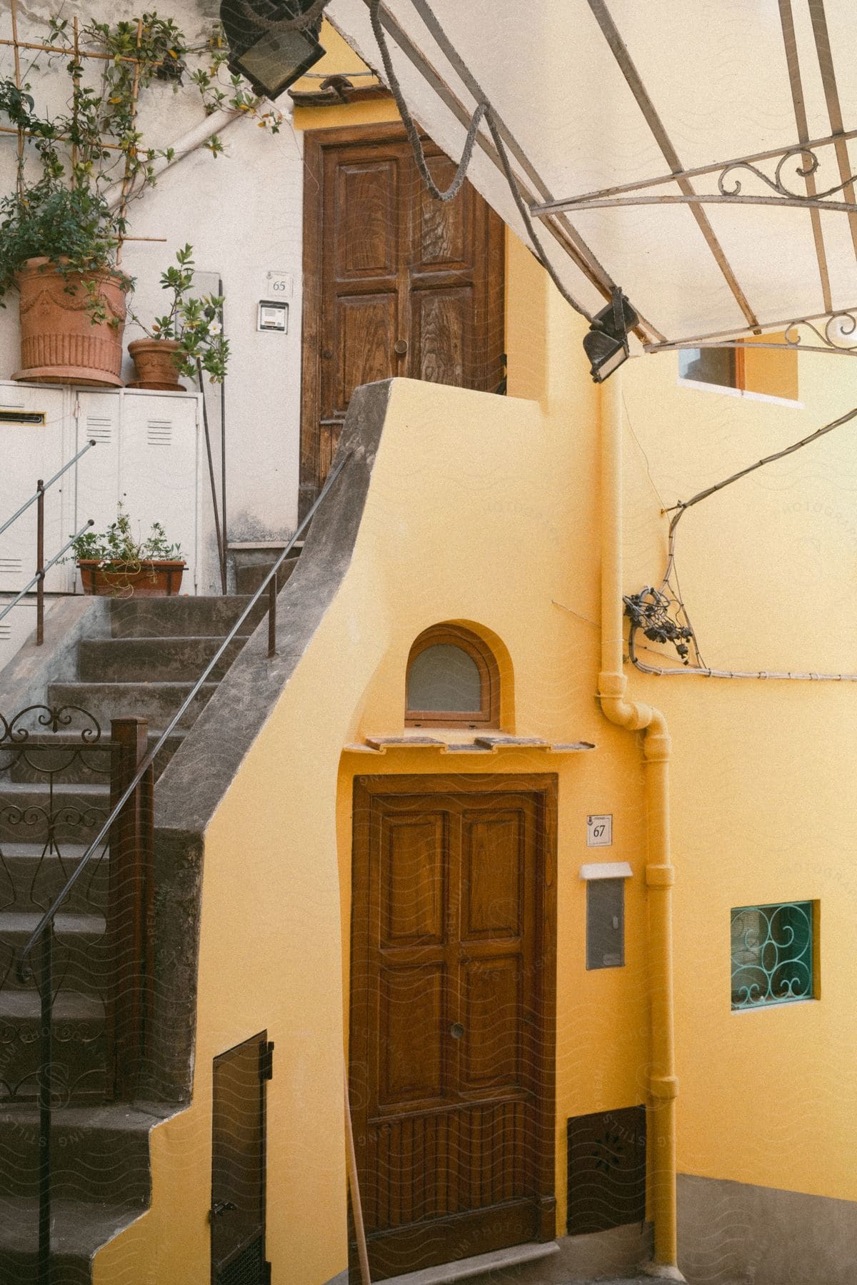 a cement outdoor staircase leading up to a closed wooden door with a metal handle of a yellow house.