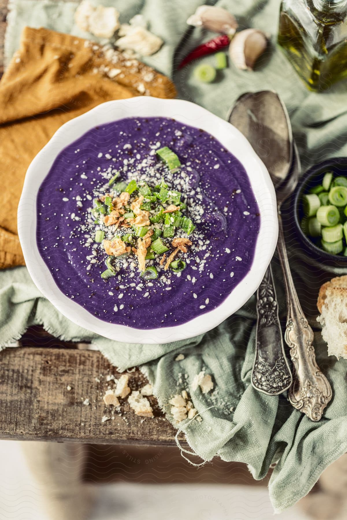 A bowl of purple soup garnished with herbs and nuts rests on a cloth-covered table