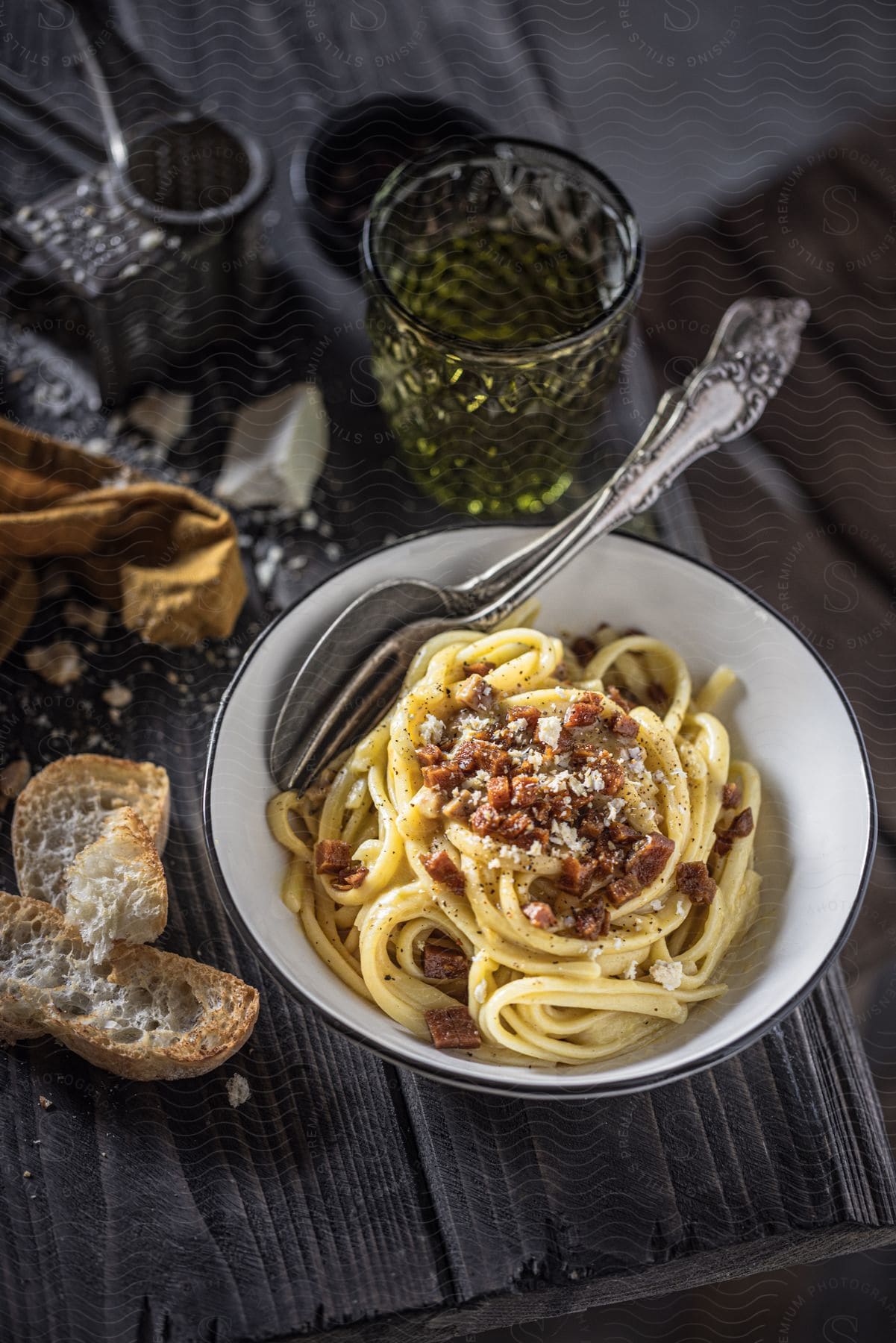 A plate of pasta carbonara garnished with bacon and cheese, served with bread and a drink.