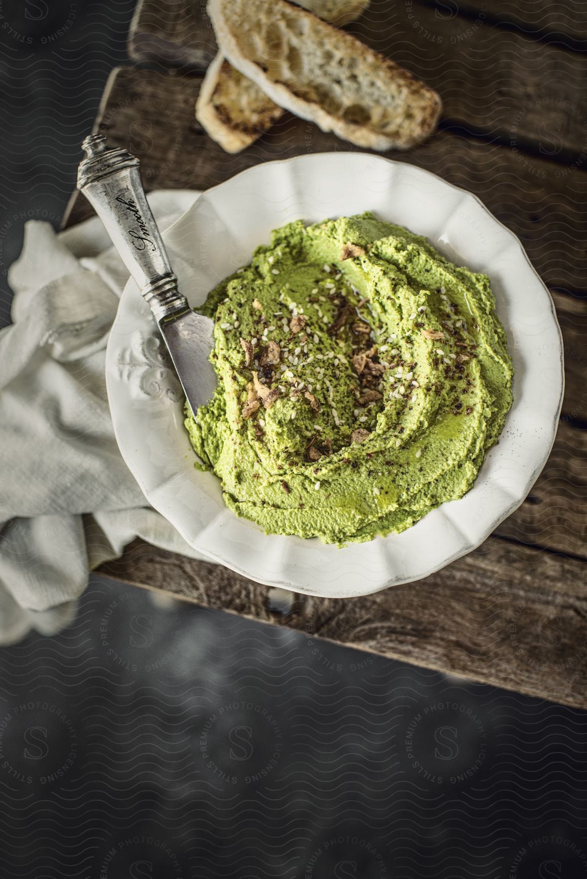 A plate of green hummus on a wooden table. The hummus is vibrant and decorated with spices.