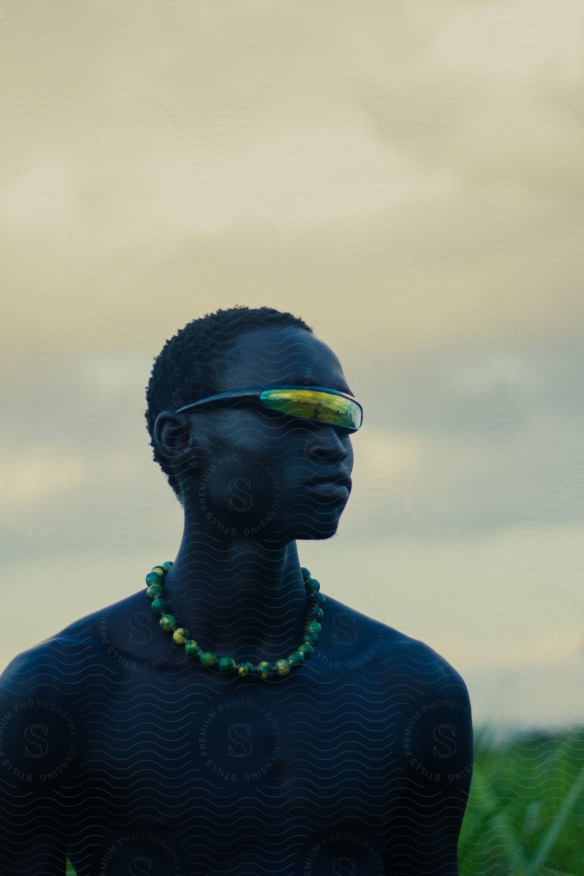 a man standing in a field wearing Rave Glasses and a yellow beads necklace.