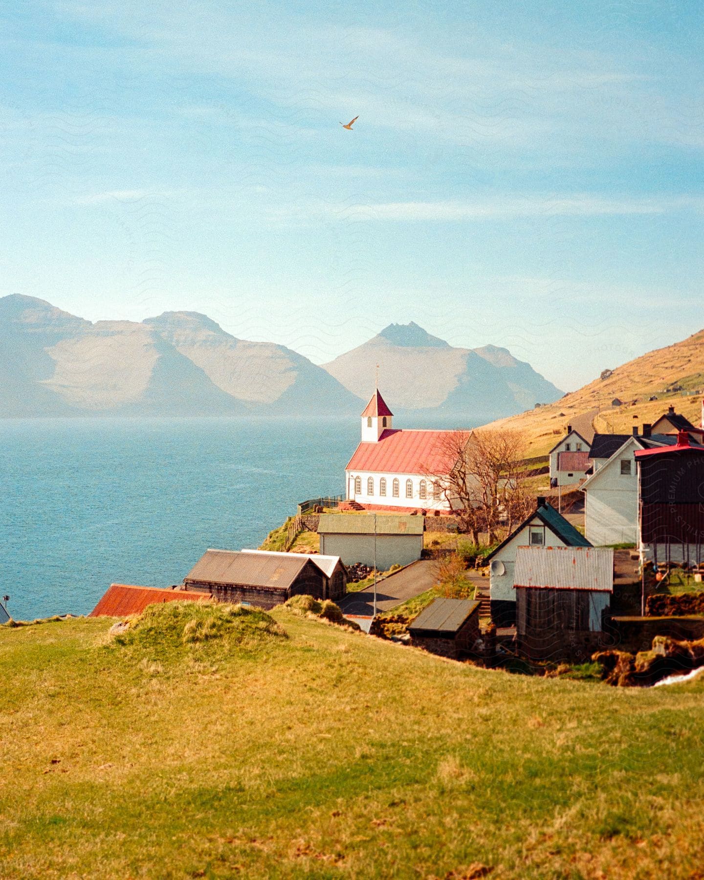 A white church with a red steeple sits on a hill overlooking a blue lake with mountain range in the background