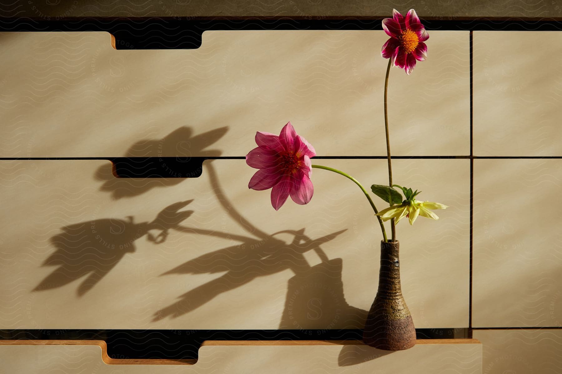 Three flowers in a rustic vase sitting on an open dresser drawer.