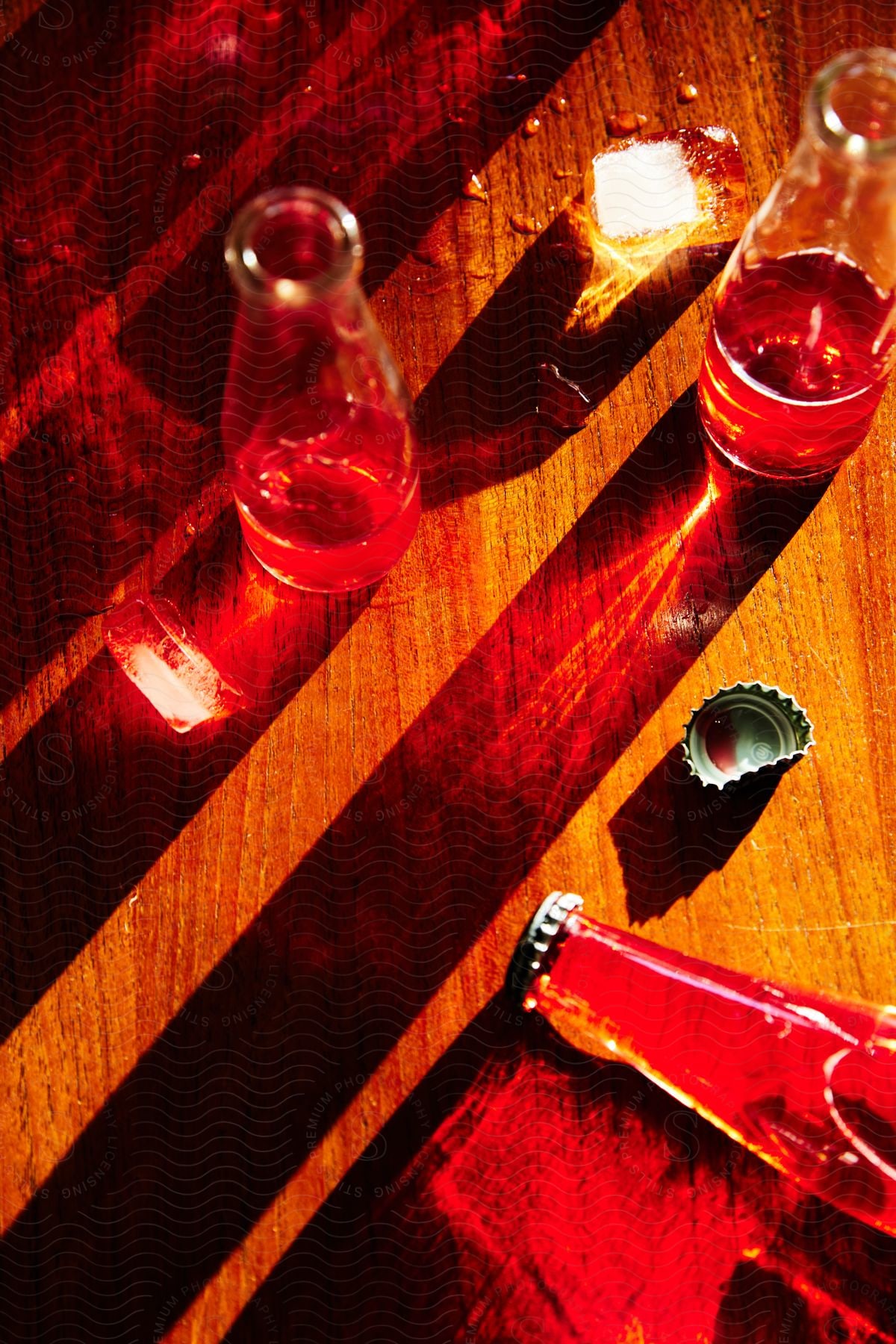 A wooden table with three bottles and a bottle cap casting red reflections