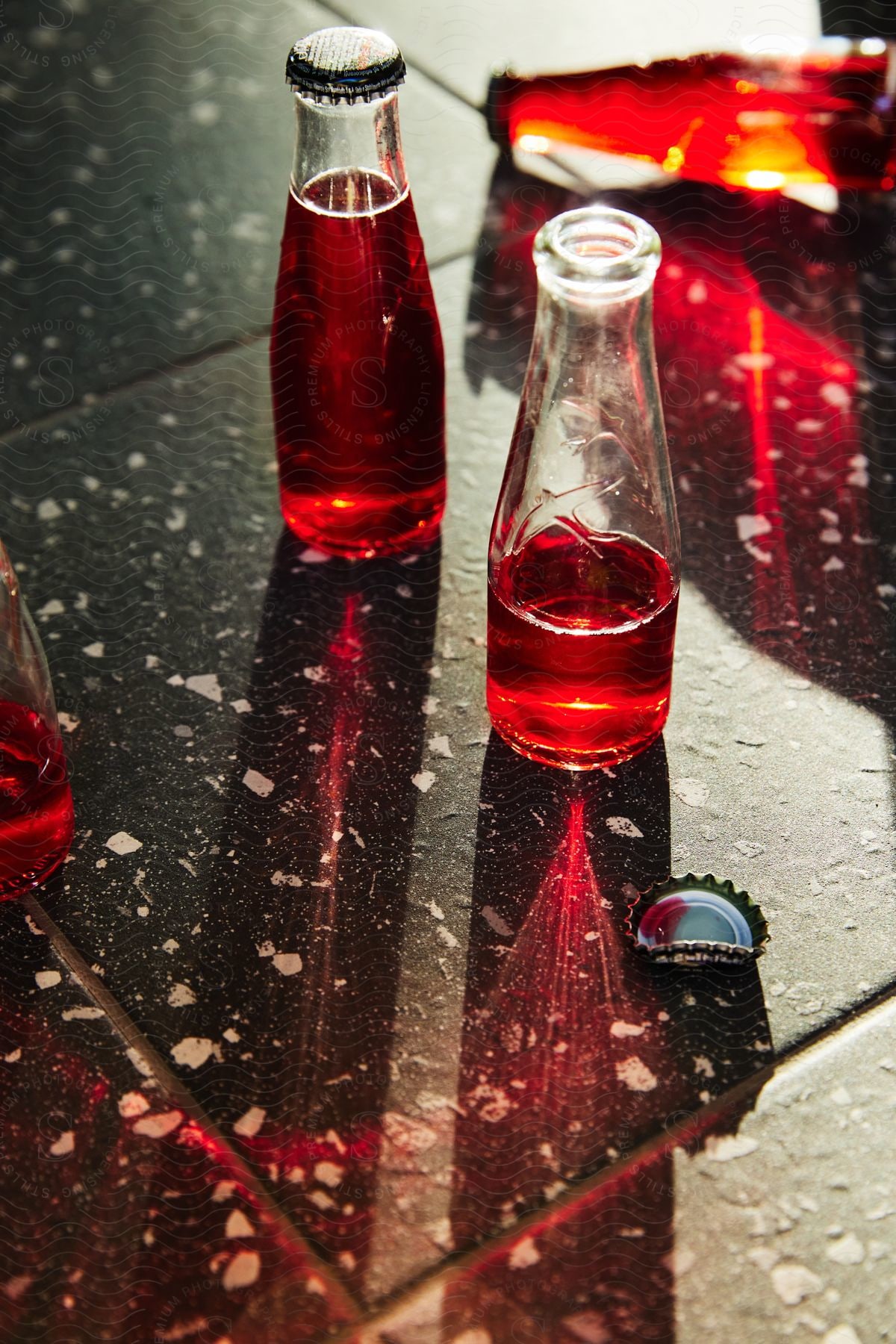 Glass bottles with a red liquid on a reflective surface with stains.