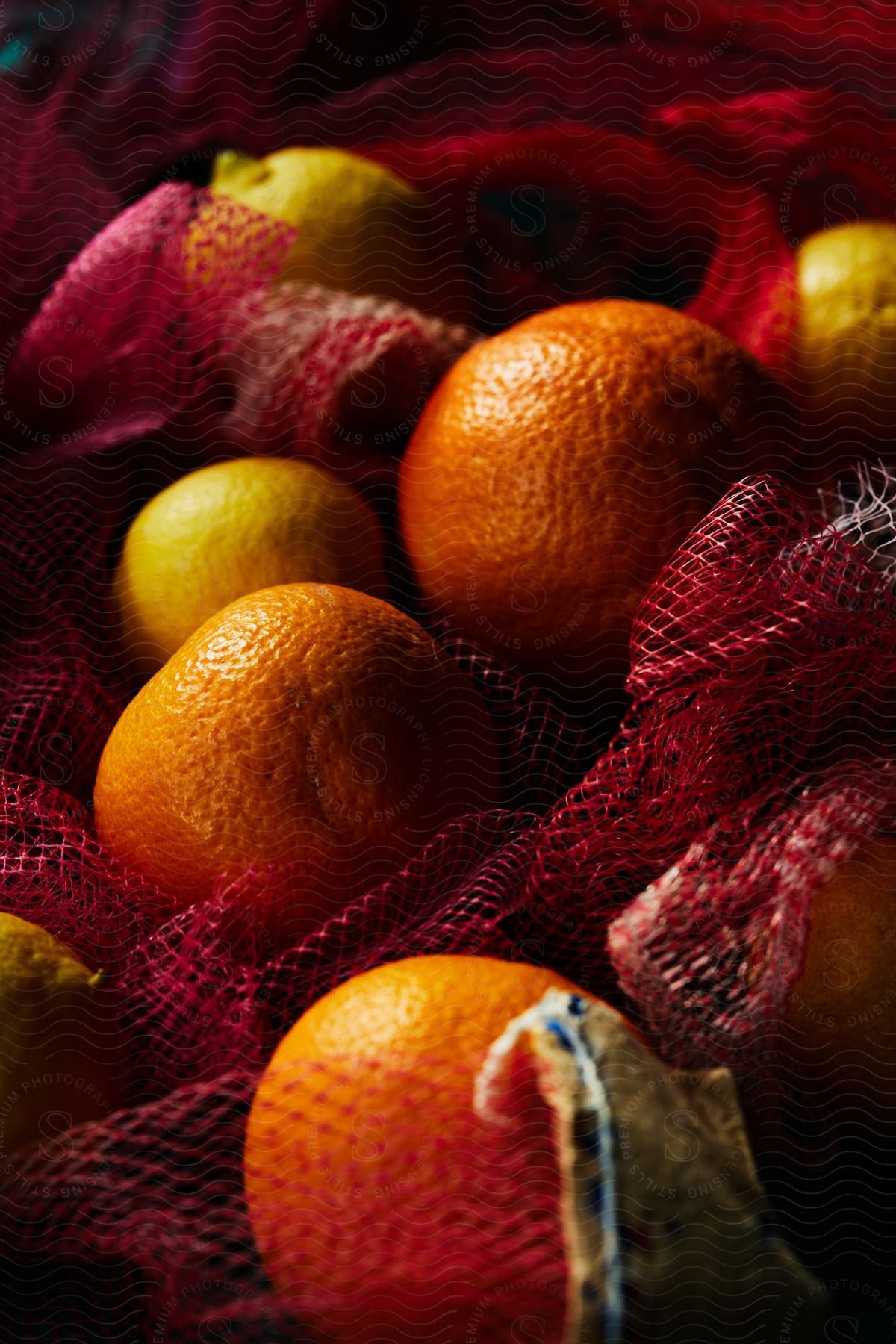 Several oranges and lemons are laying on top of a red mesh bag.