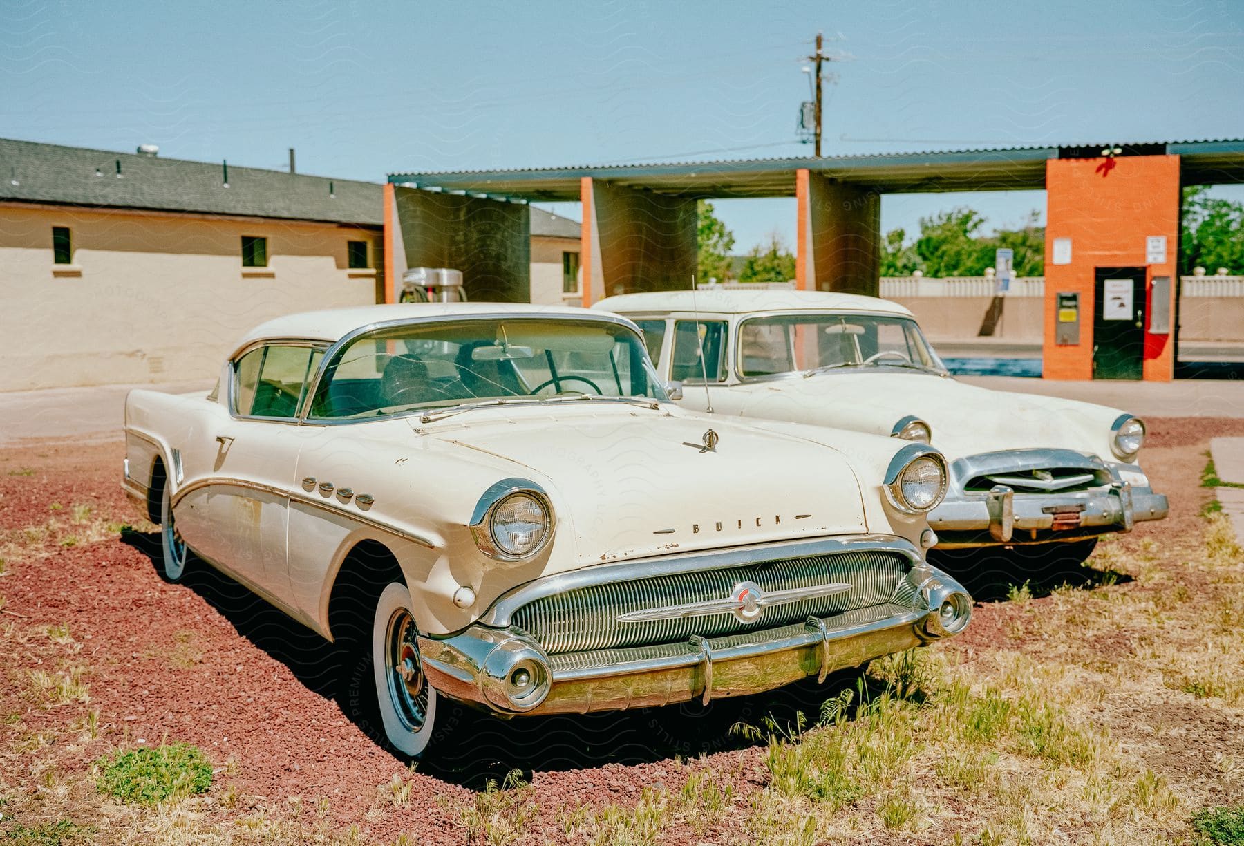 Two white 1957 Buick Modelljahr parked side by side in a dirt lot.