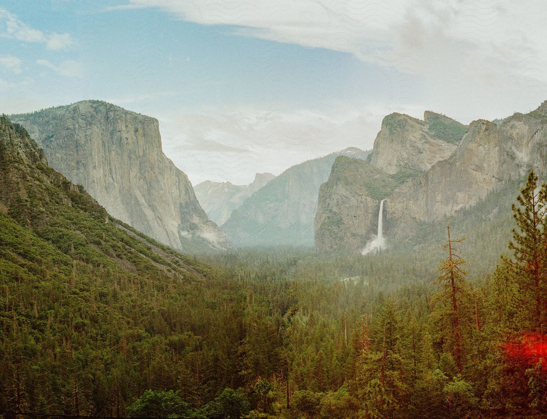 Yosemite National Park’s  Lower Yosemite Fall plunging into a deep pool surrounded by lush greenery and rocky cliffs.