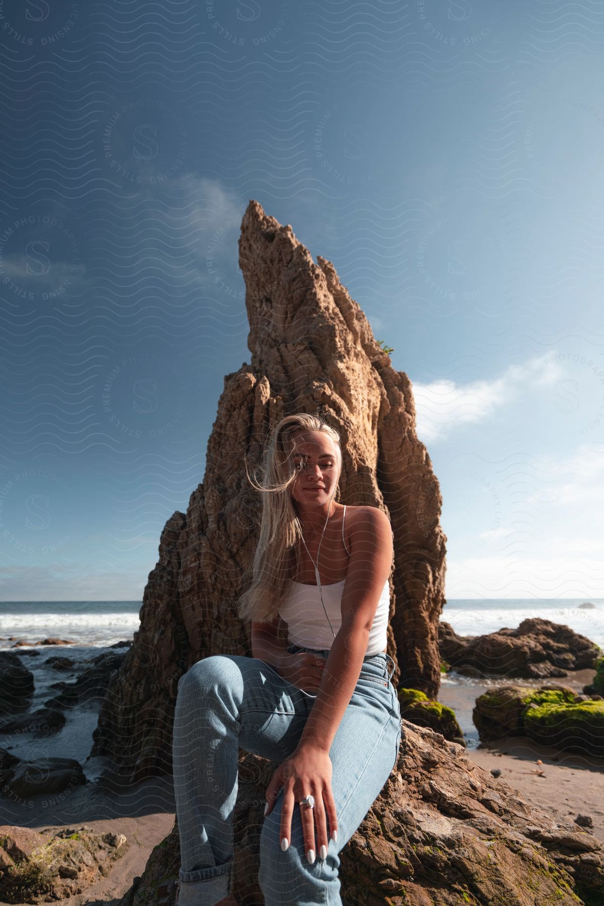 Young blonde woman sitting near a rock formation on the beach