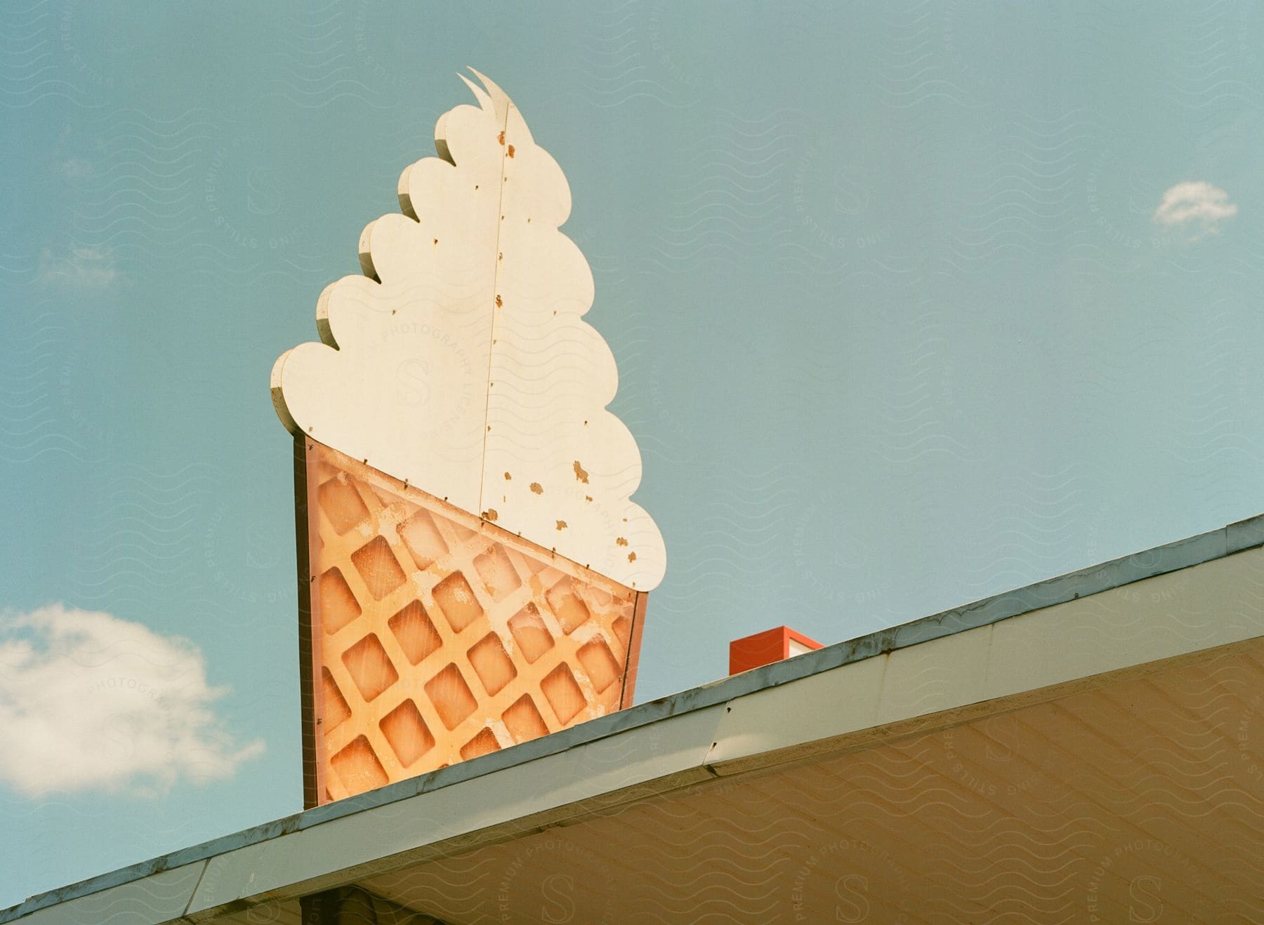 A weathered ice cream cone sign stands tall atop a fast food restaurant, bathed in the warm glow of a sunny day.