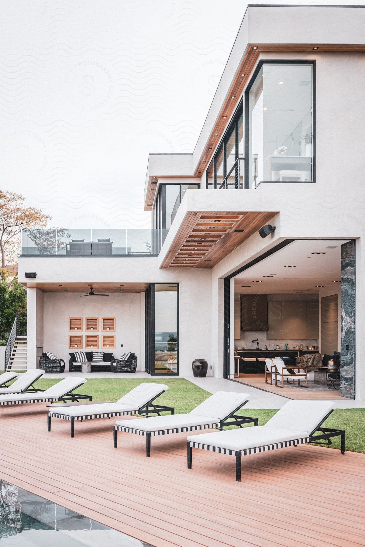 A house of modern architecture with a grassy backyard and six white sunbathing chairs