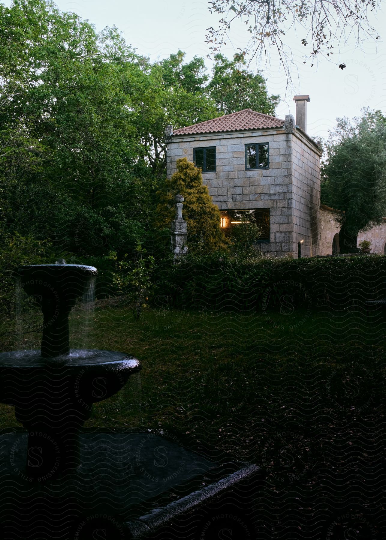 Fountain in the back yard with hedges and trees near the house