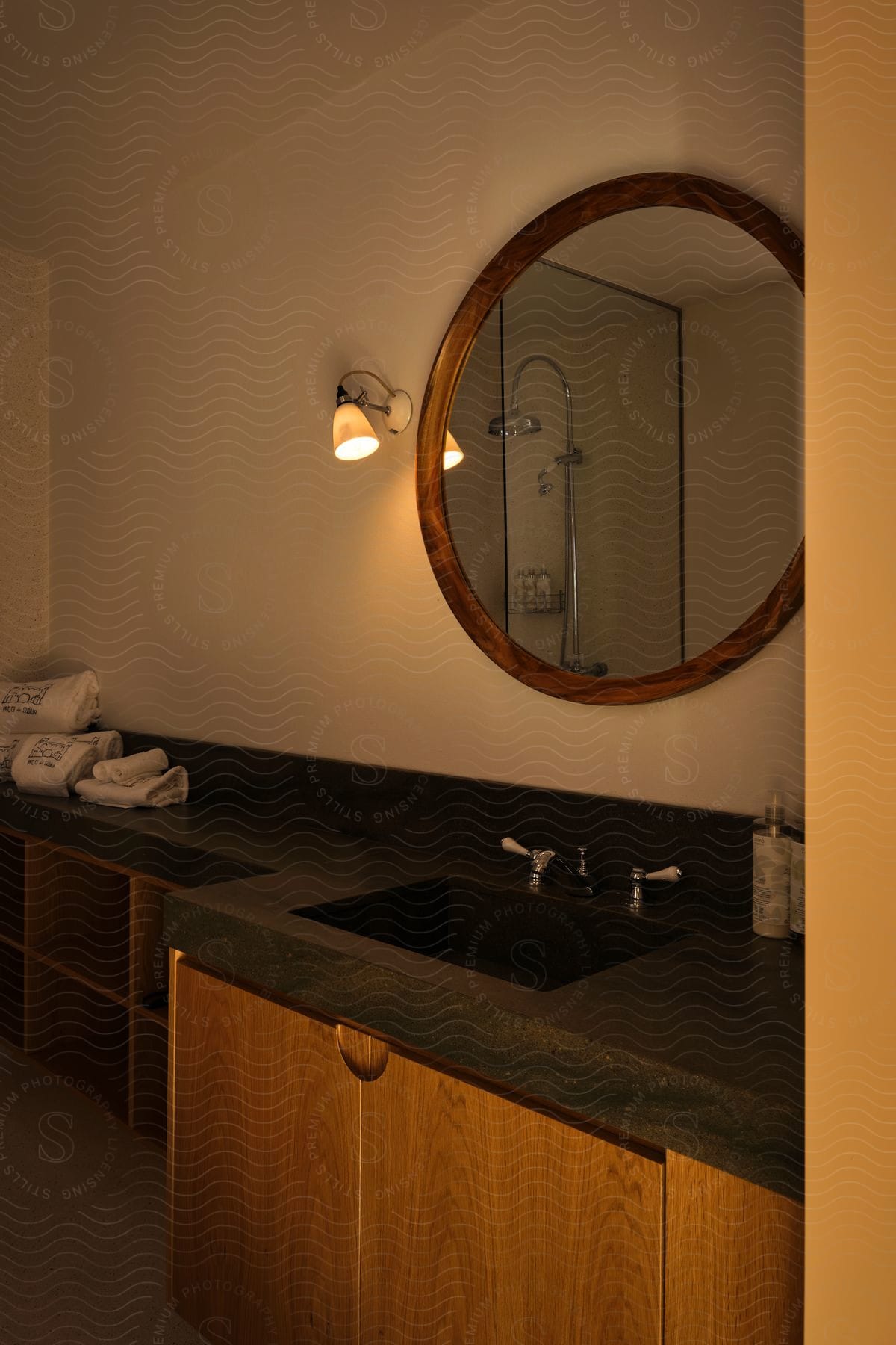 A bathroom with a dark marble sink and an oval mirror on the wall reflecting the image of the shower