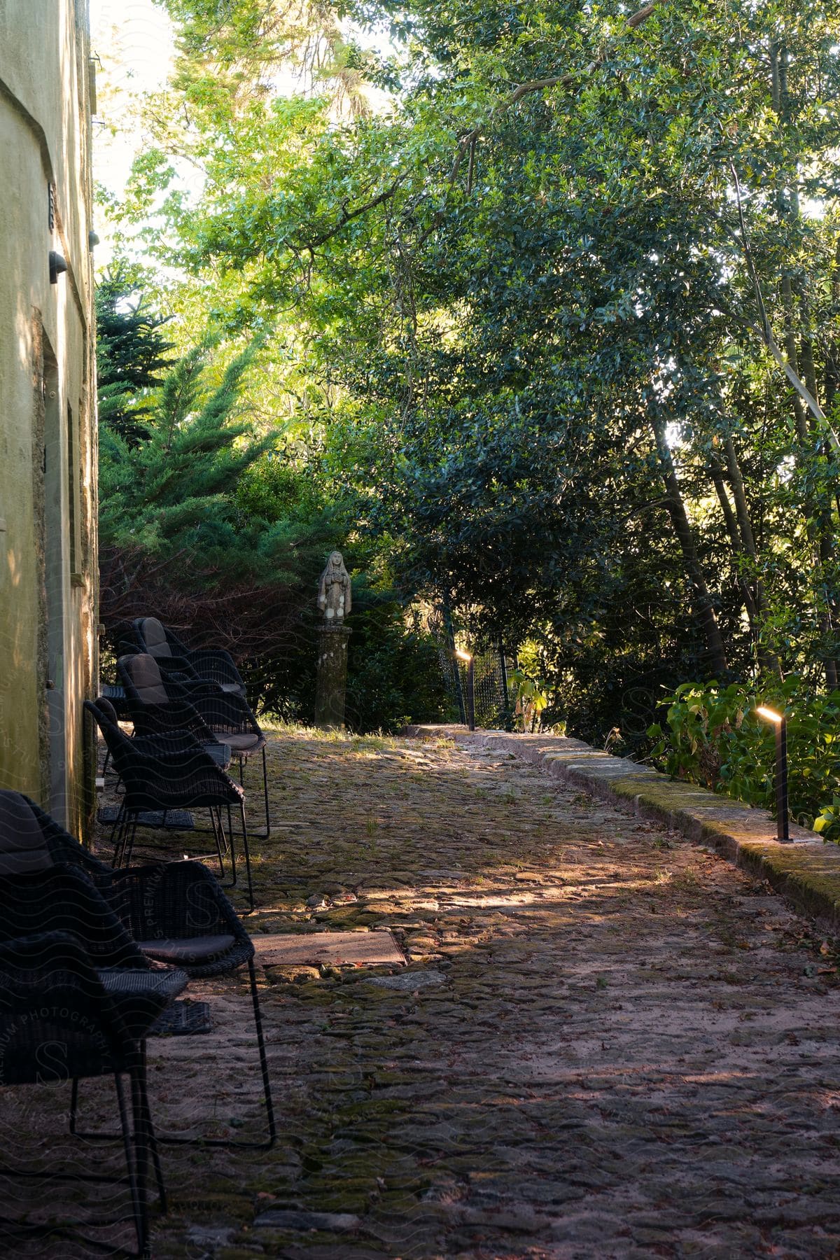 Five black chairs sit next to a house on a cobblestone driveway on a summer day.