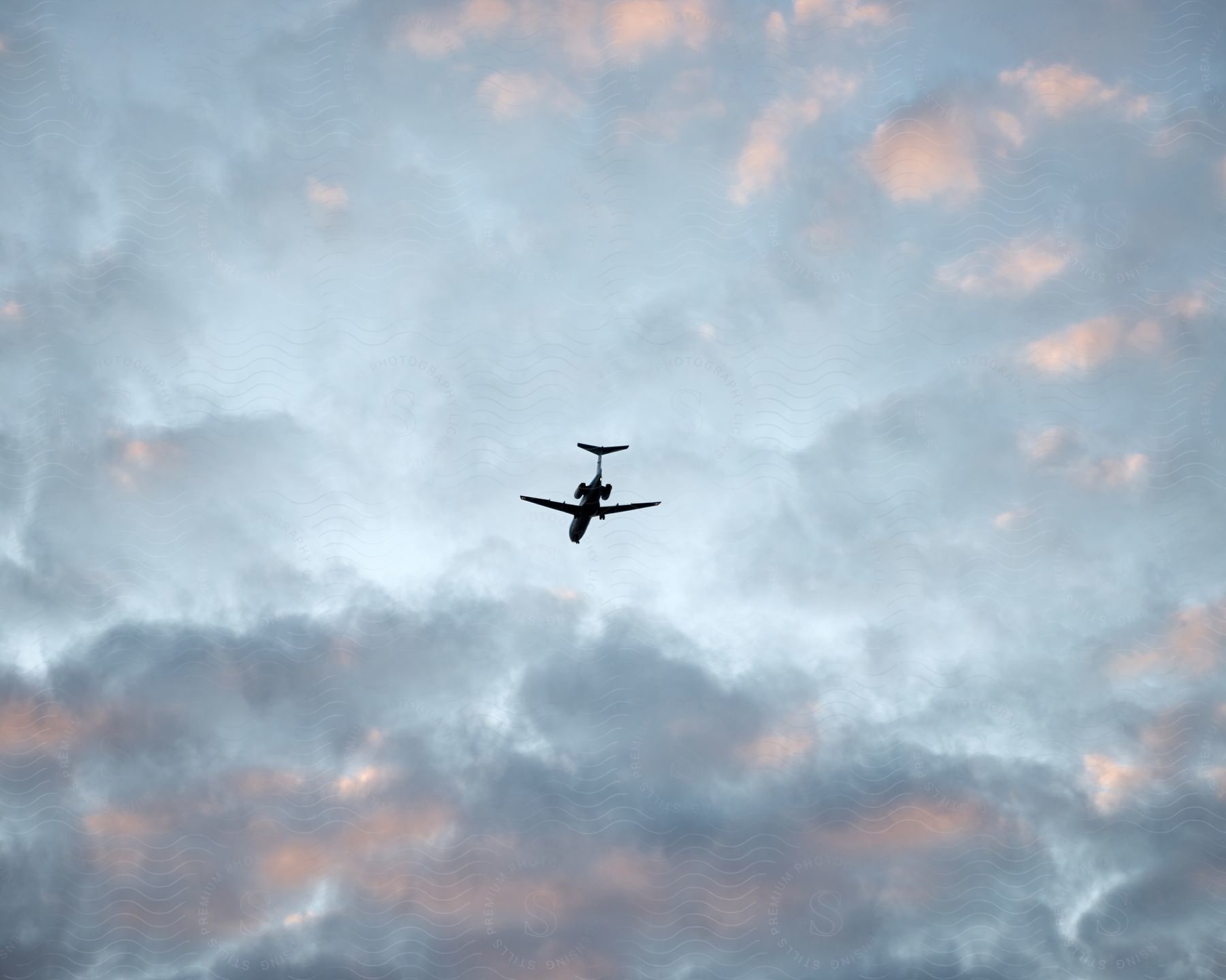 A commercial plane flying over the sky that has gray clouds with reflections of sun rays