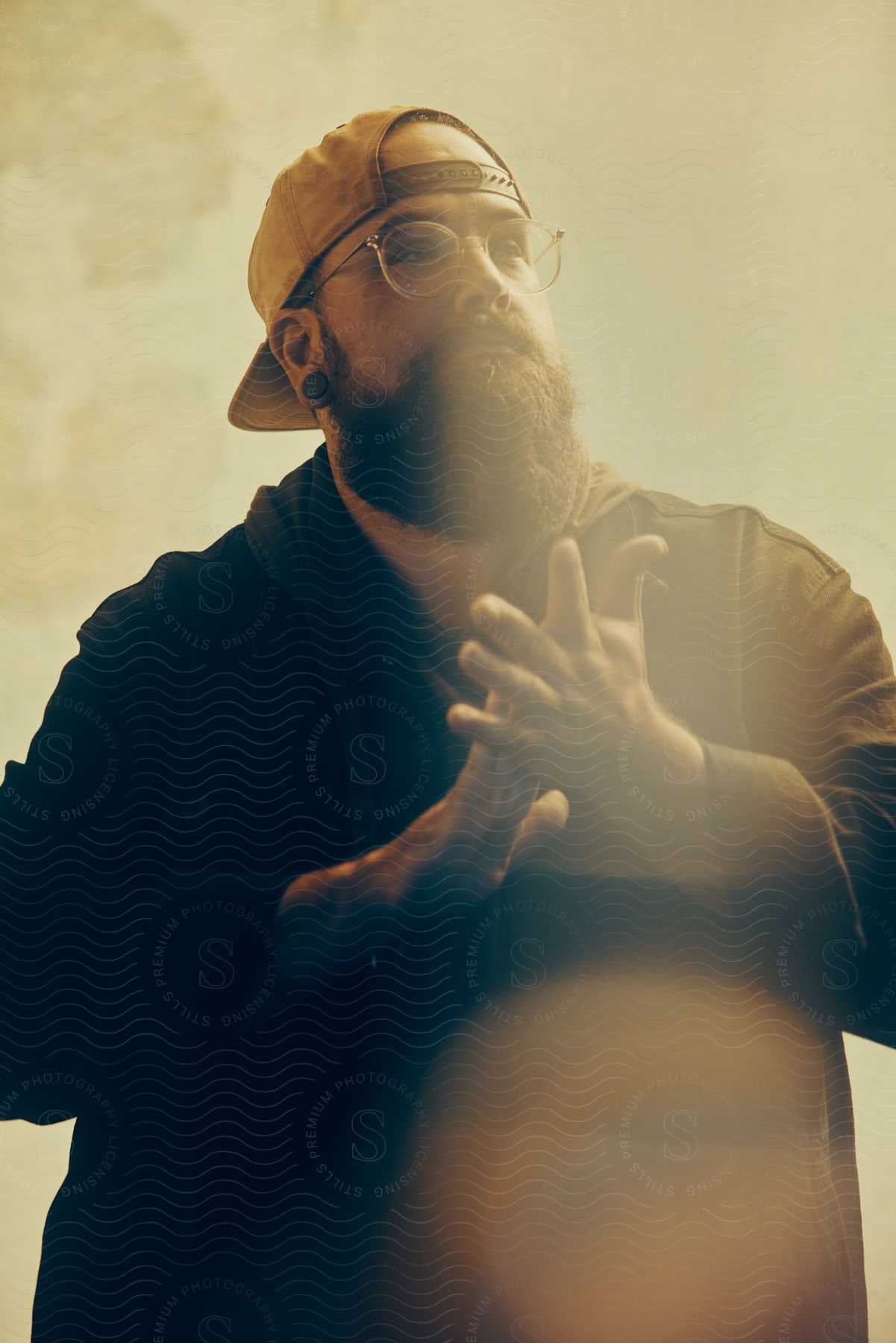 Young bearded man wearing a backwards baseball cap rubs his hands looking up