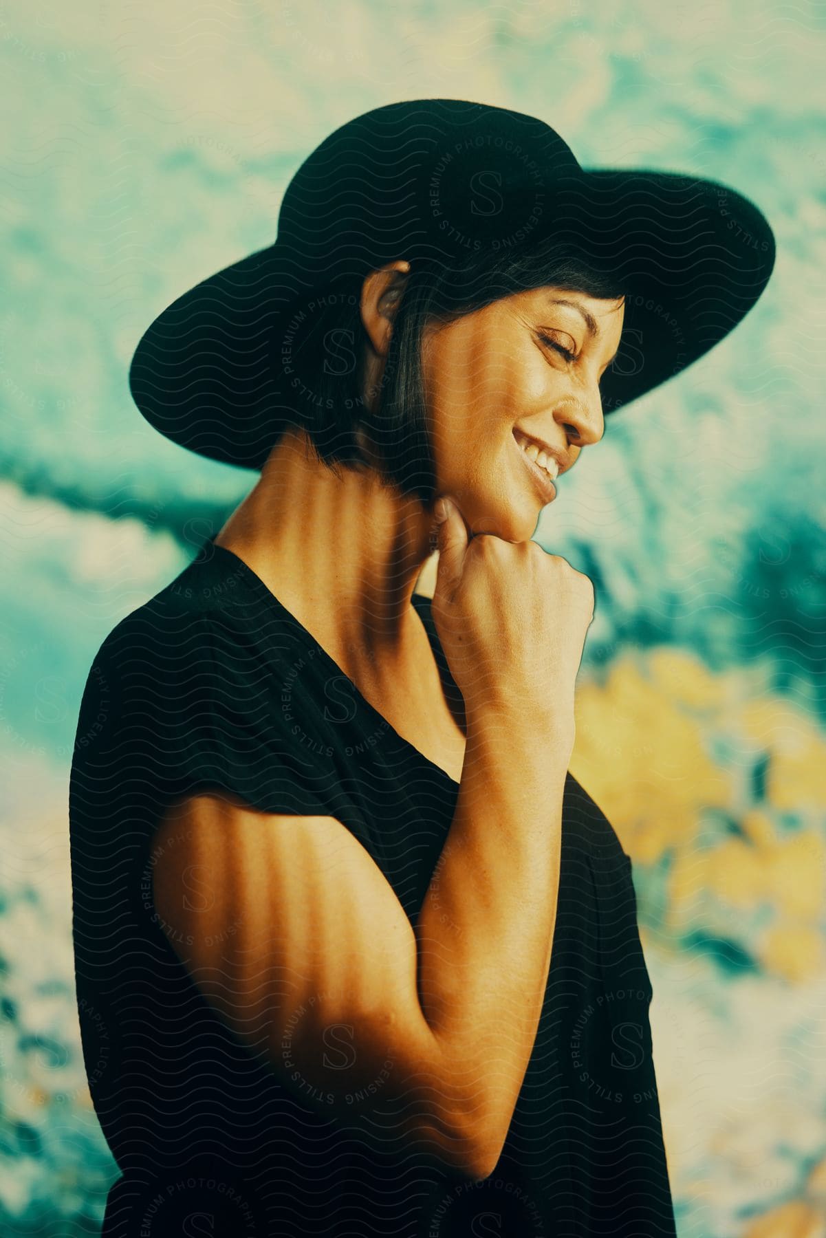 A woman in a black hat and tshirt poses in front of a colored background