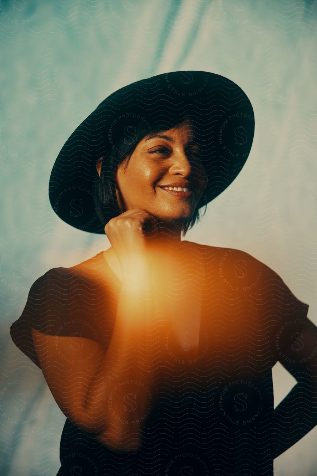 A young woman wearing a black blouse and hat smiles in the sunlight