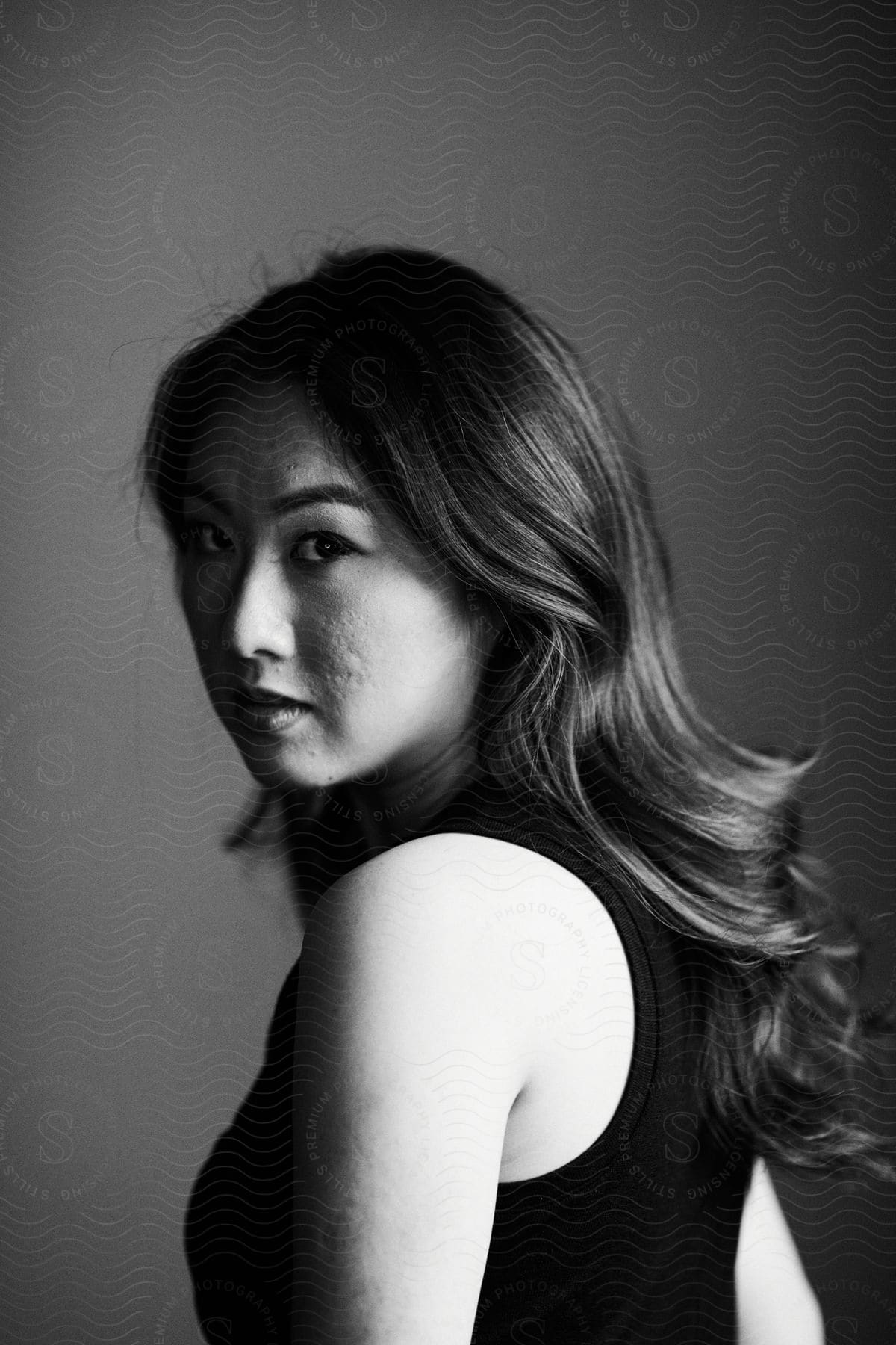 A woman in a black tank top captured in black and white slightly turned and looking at the camera