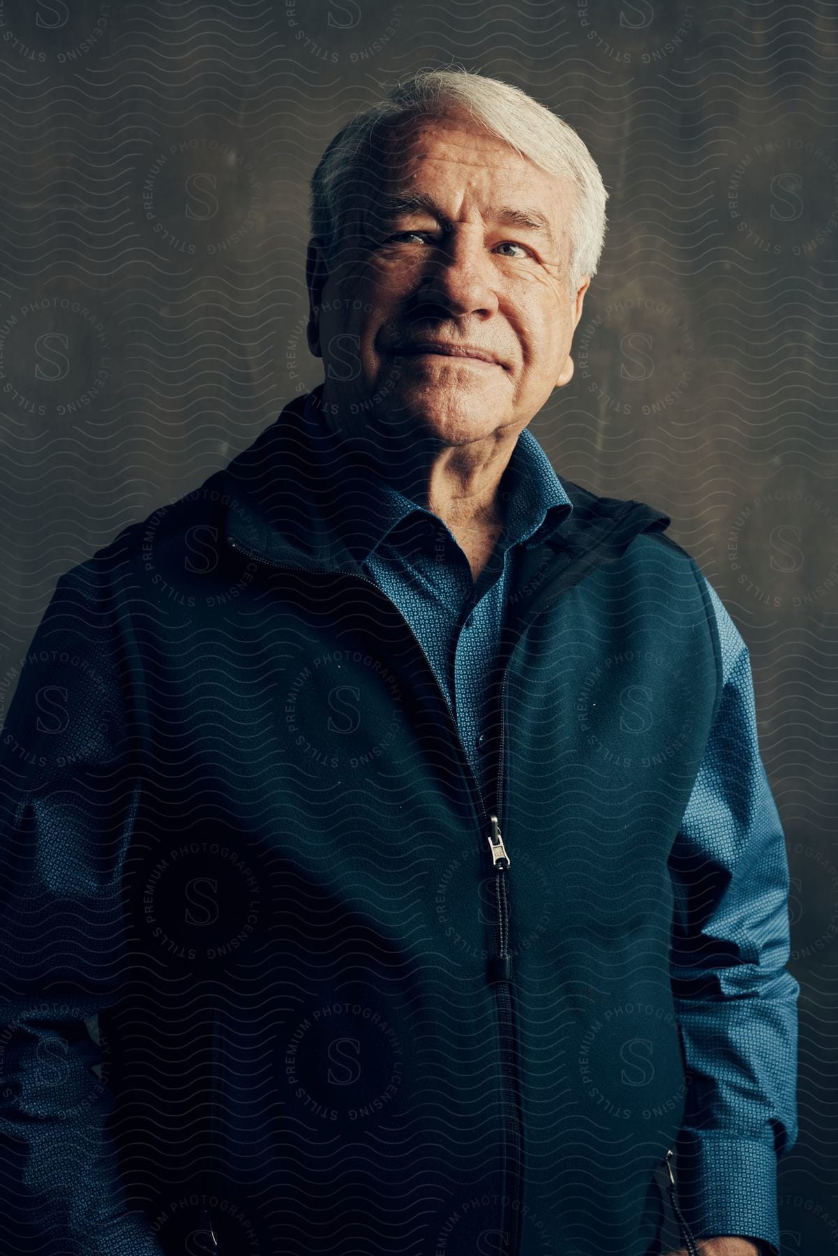 A man wearing a blue shirt and a vest with a zipper standing with his arms to his sides