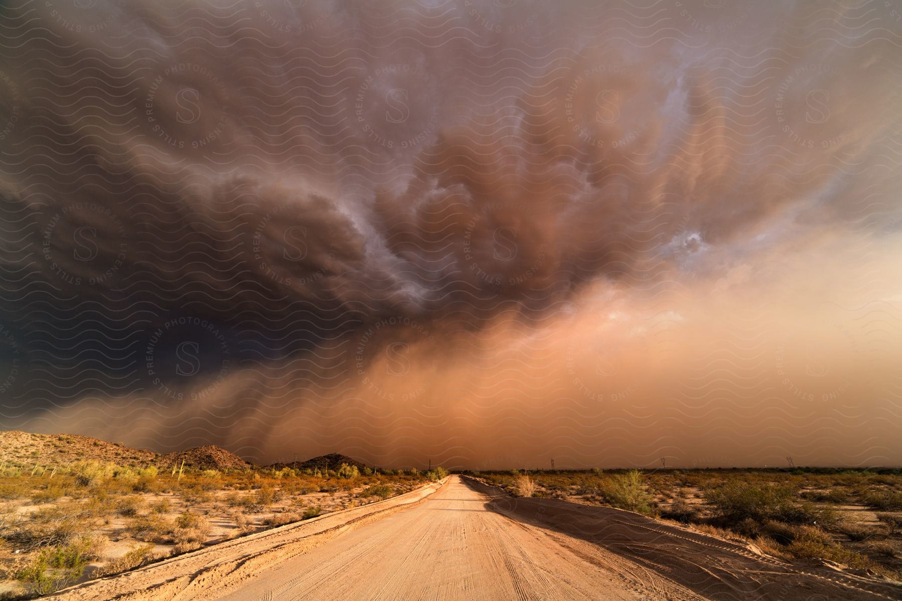 A dirt road stretches into the distance towards storm clouds