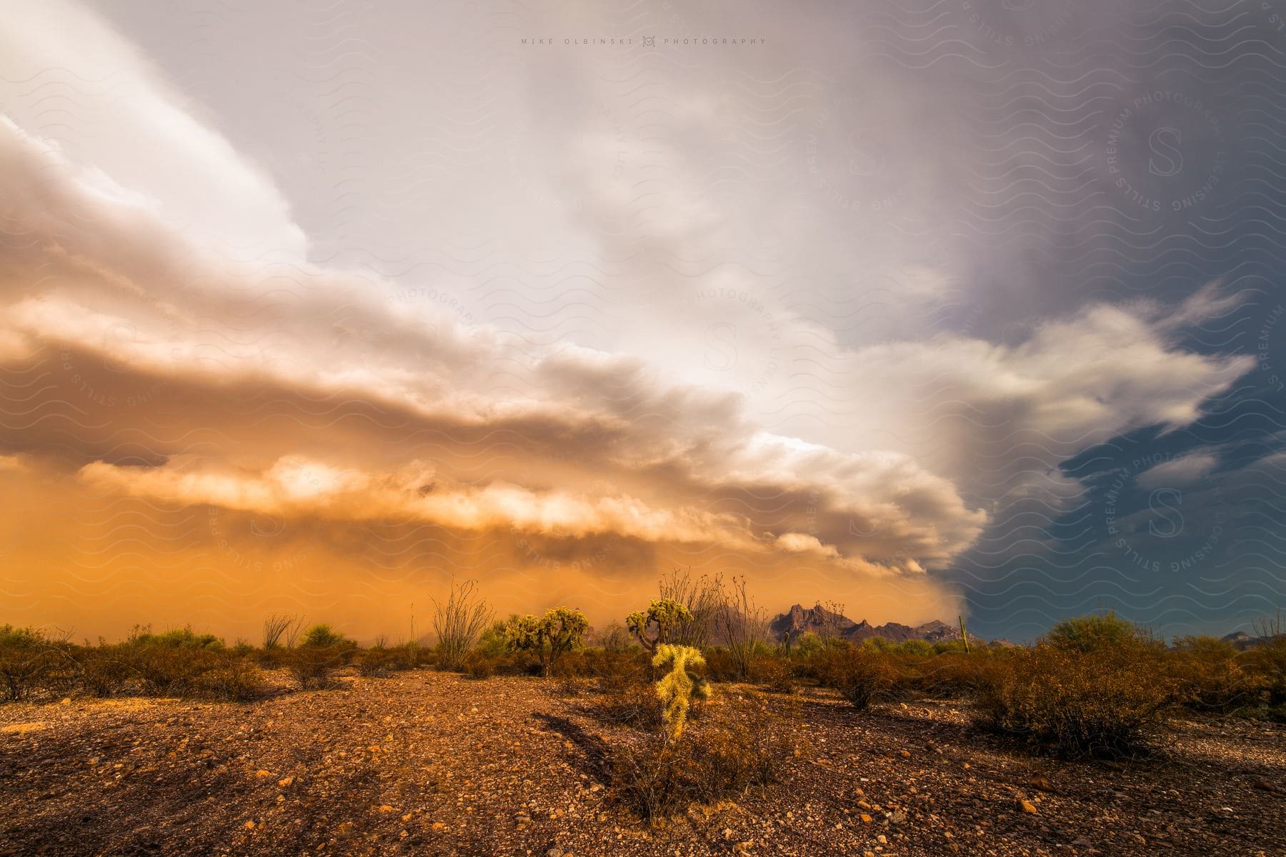 A colorful cloud with dark white and blue colors hovering over a desert landscape with sparse grass