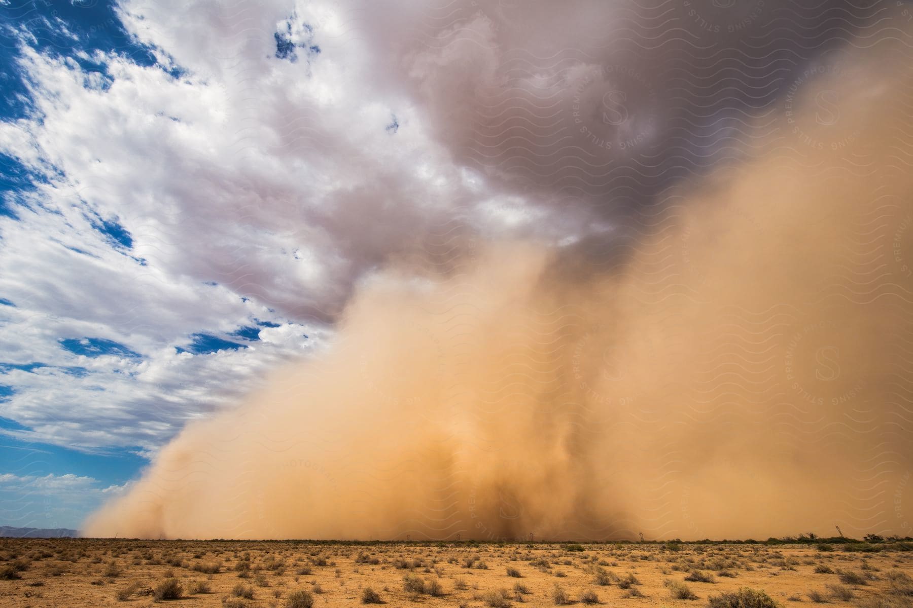 A dust storm moves across the desert land with white clouds floating in the sky overhead