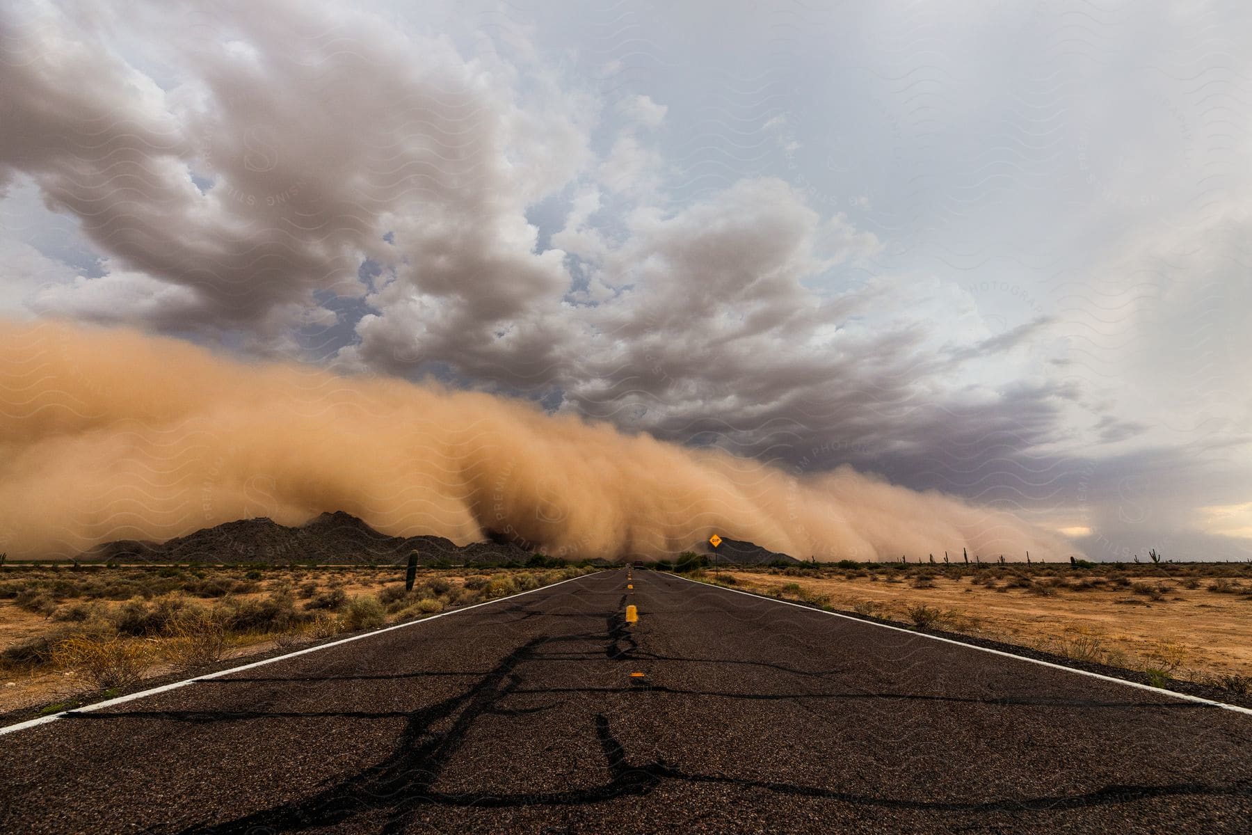 A dust storm rolls in over desert mountains at the end of a highway road under a cloudy sky