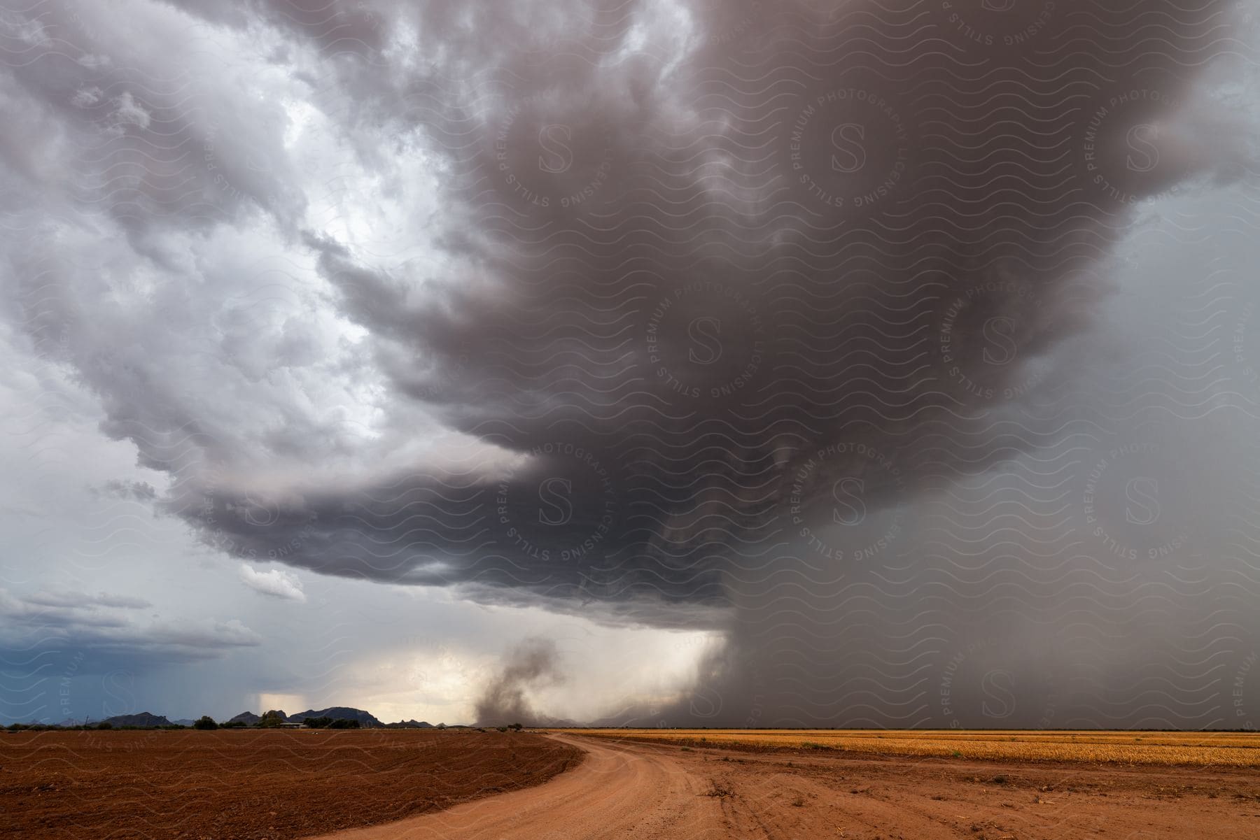 A dark supercell storm pours rain over rural land as it moves