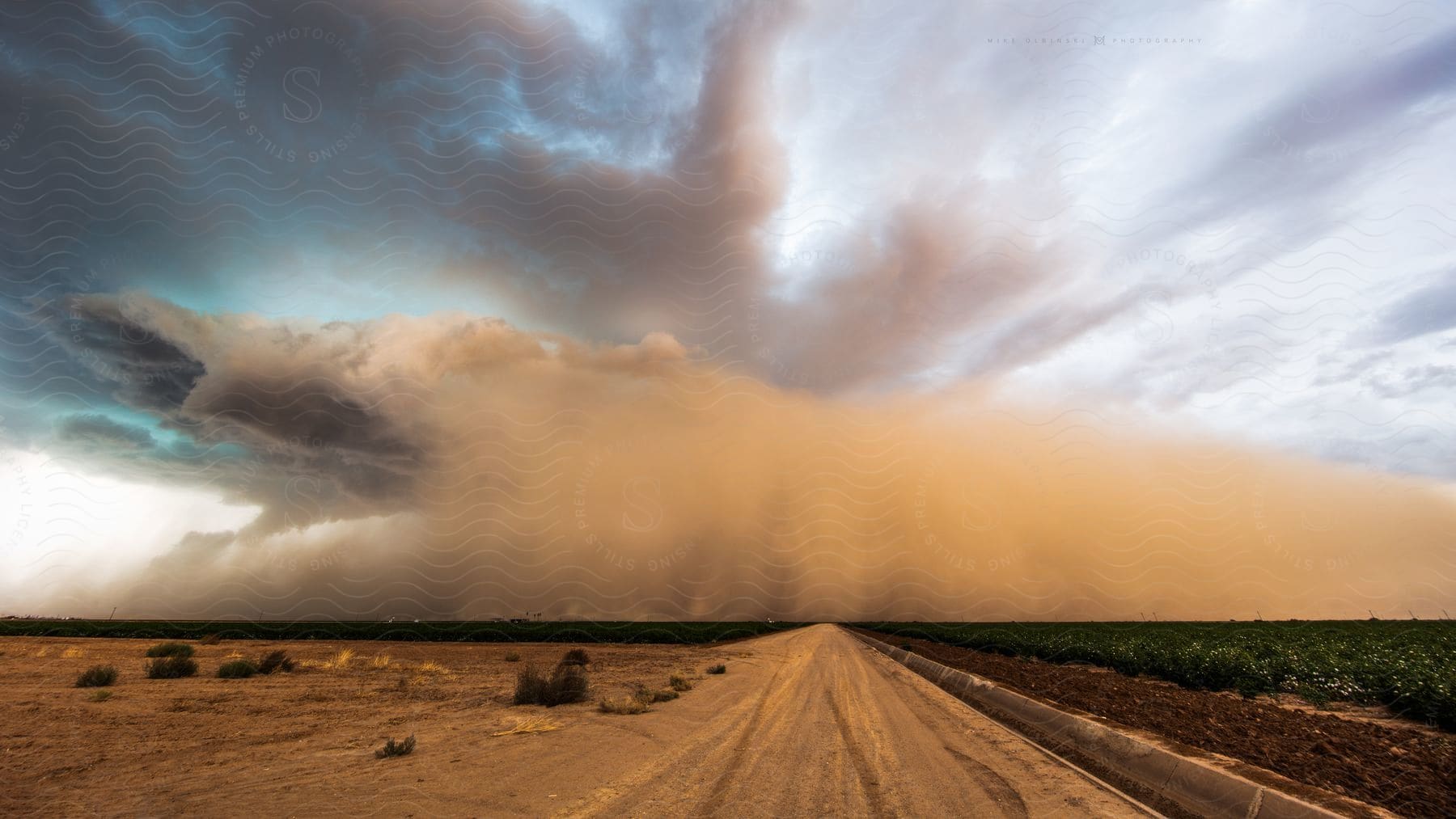 A sandstorm moves across a desert landscape along a dirt road