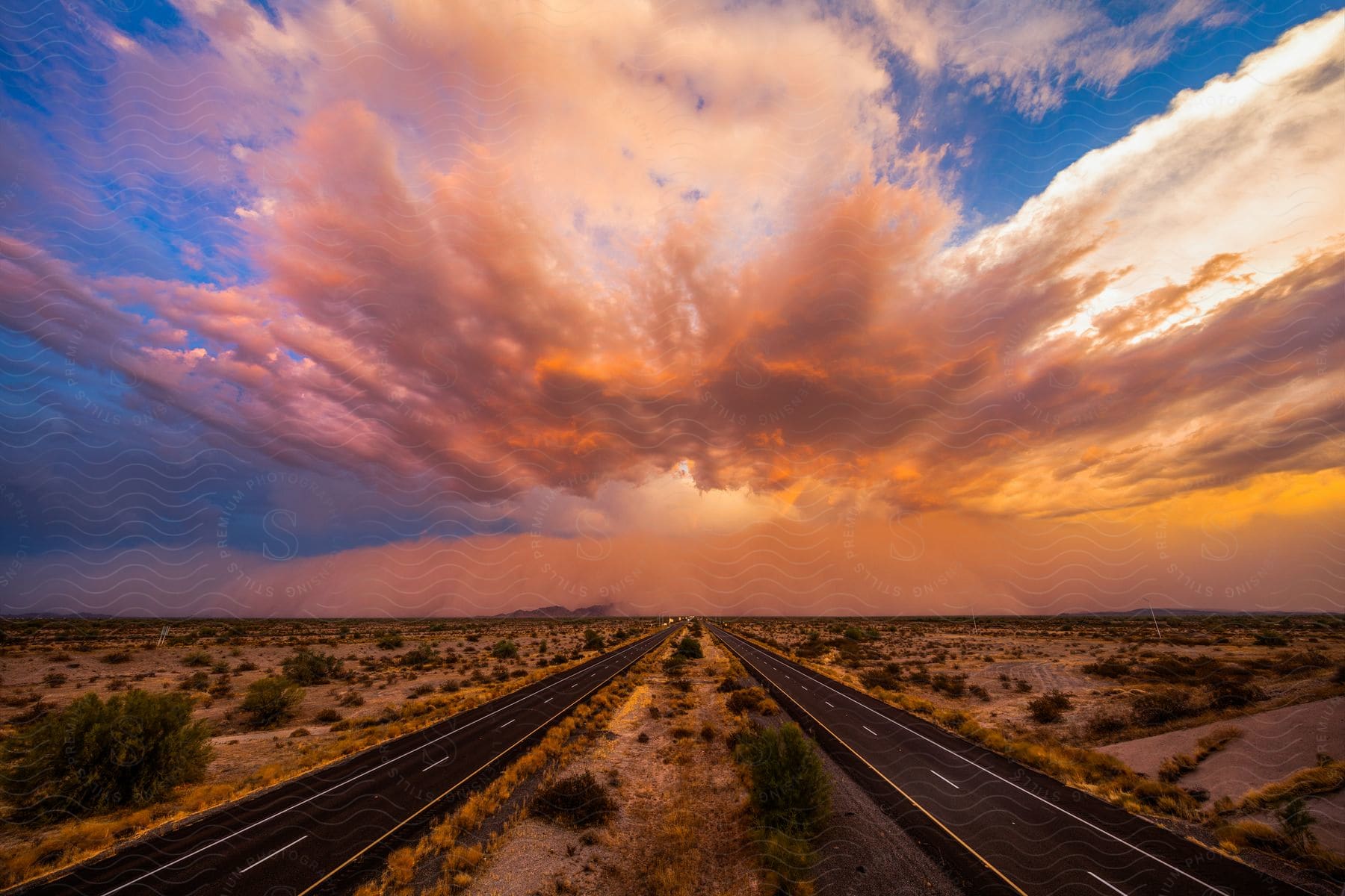 Two roads through the desert reaching the storm clouds in the horizon at sunset