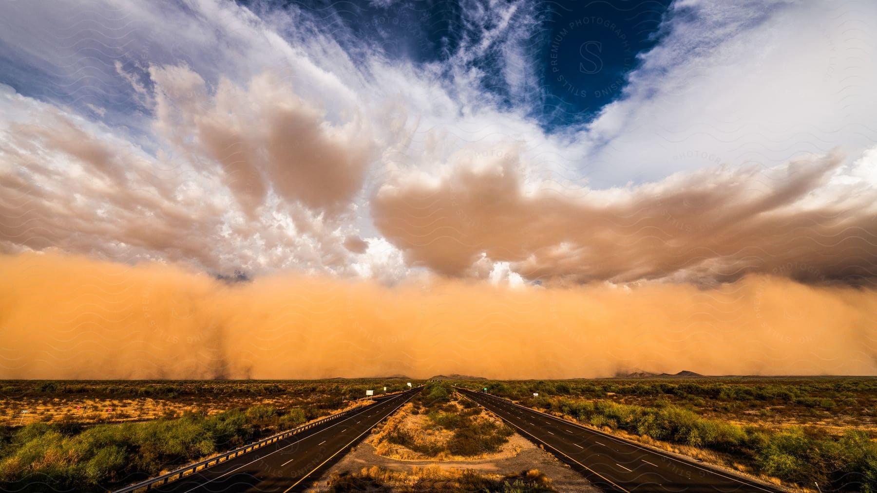 A large cloud of dust rolls across the sky over a desert highway