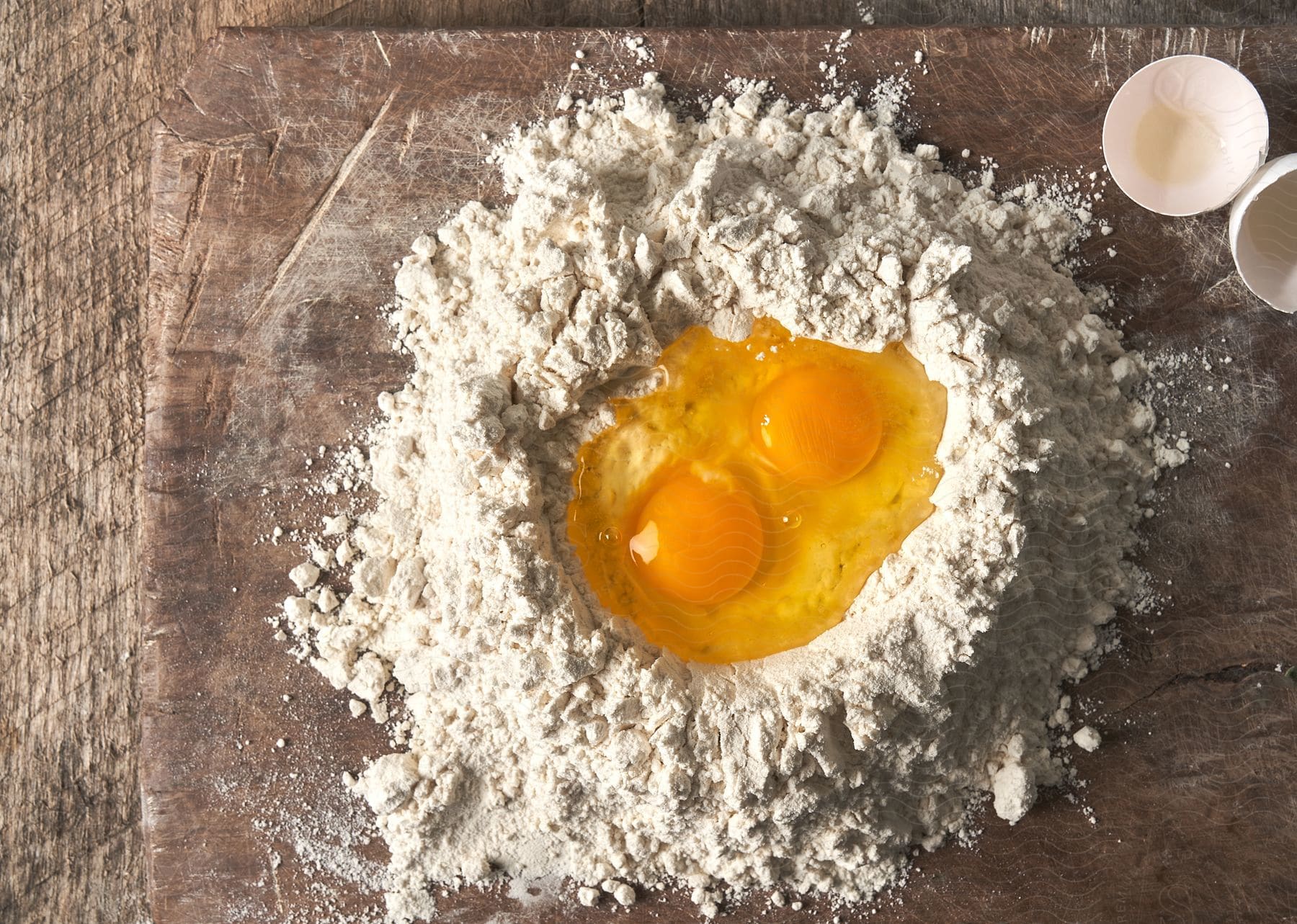 Two cracked eggs on a flour pile on a wooden surface