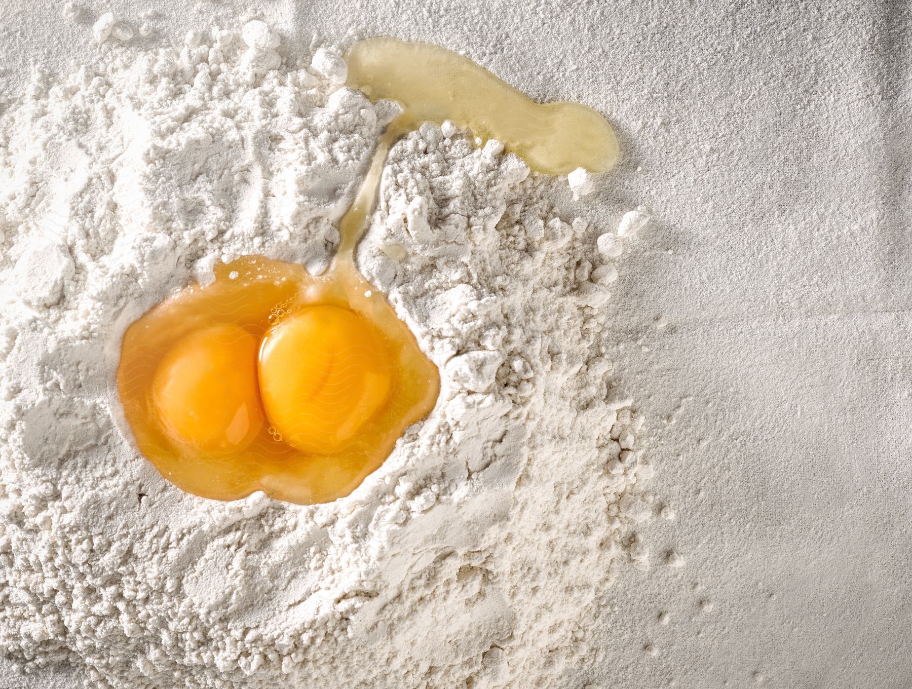 A pile of white flour and two egg yolks raw on a white cloth