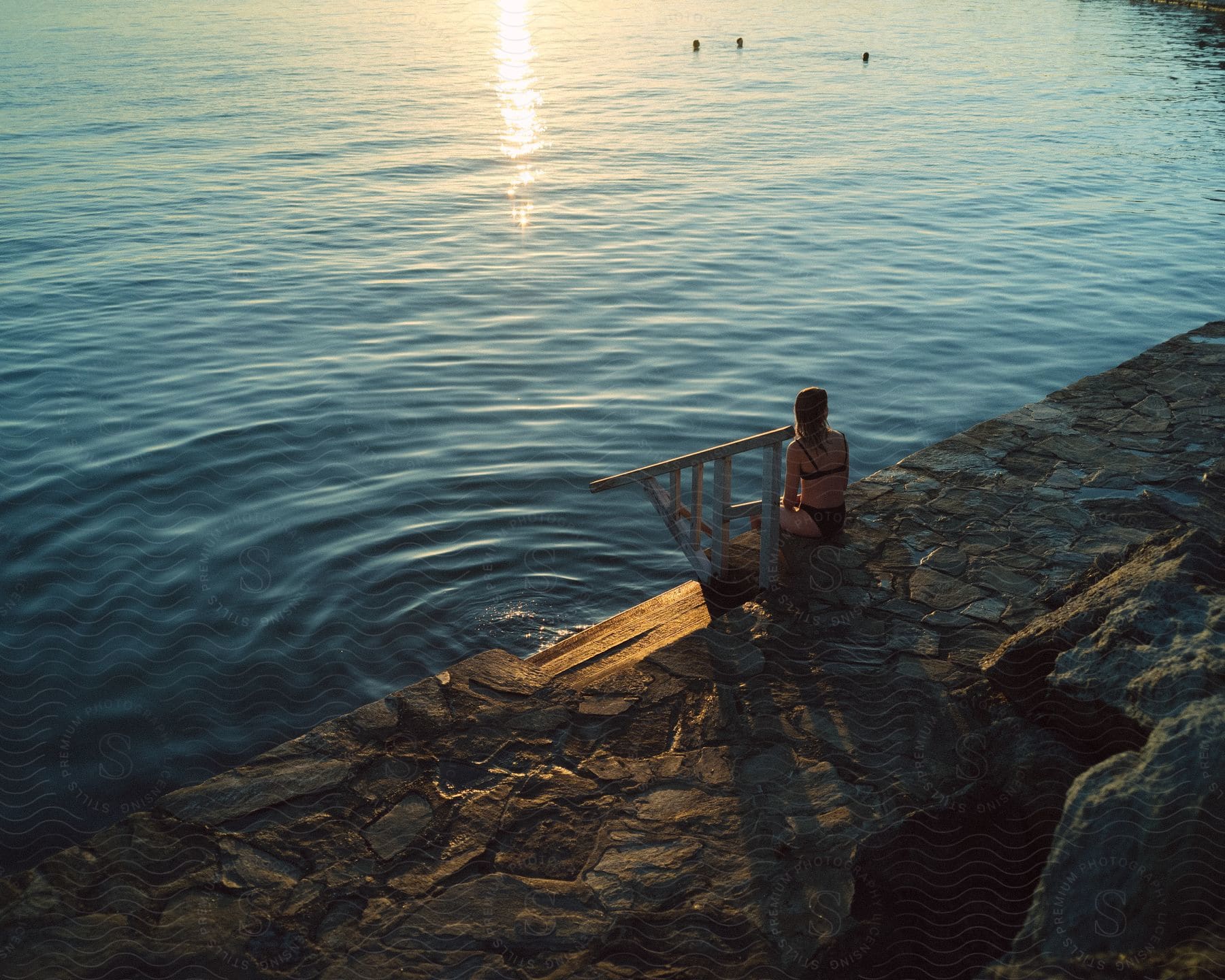 A woman sits by the water as others swim