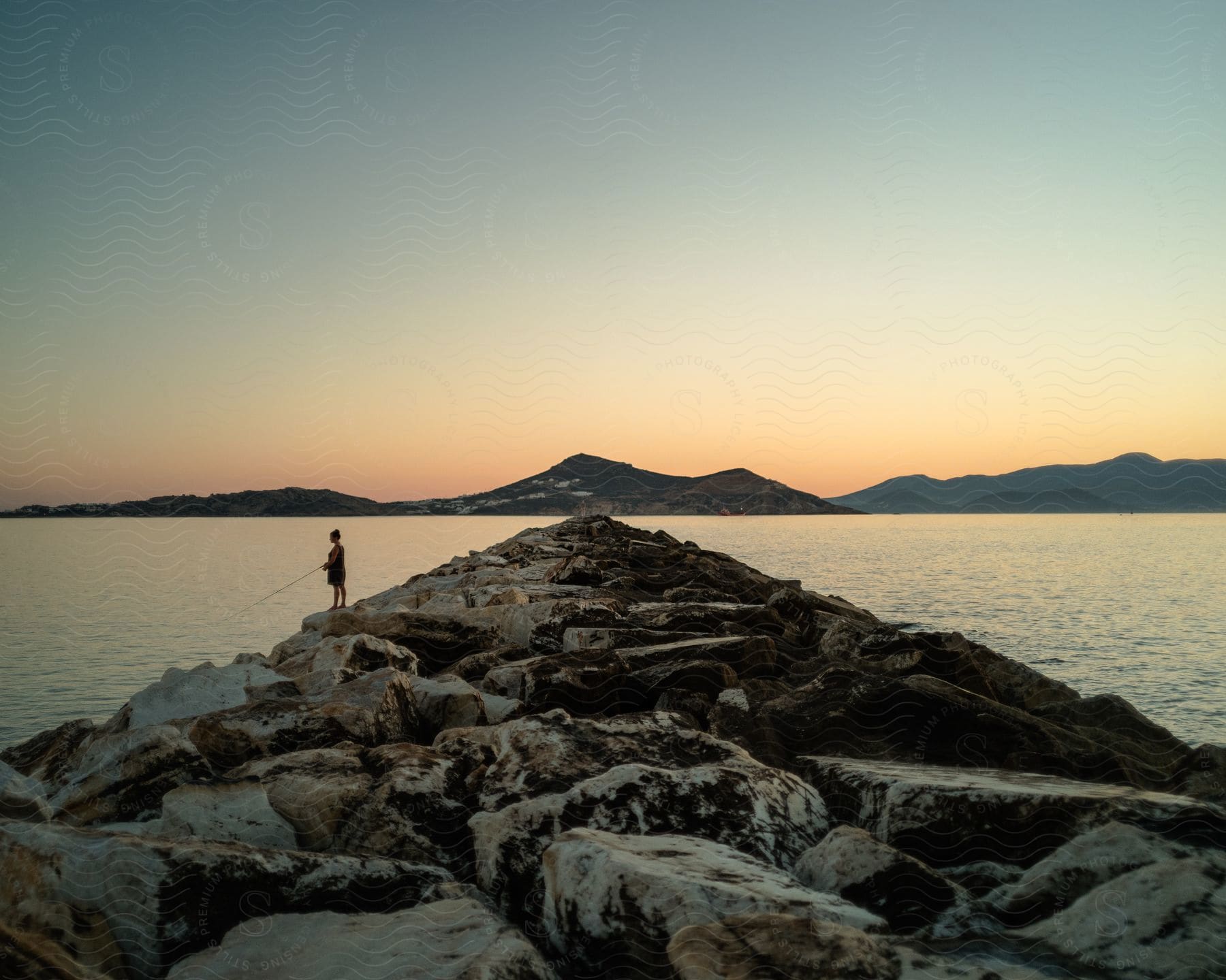 Coastal landscape with rocks and a woman fishing during sunset