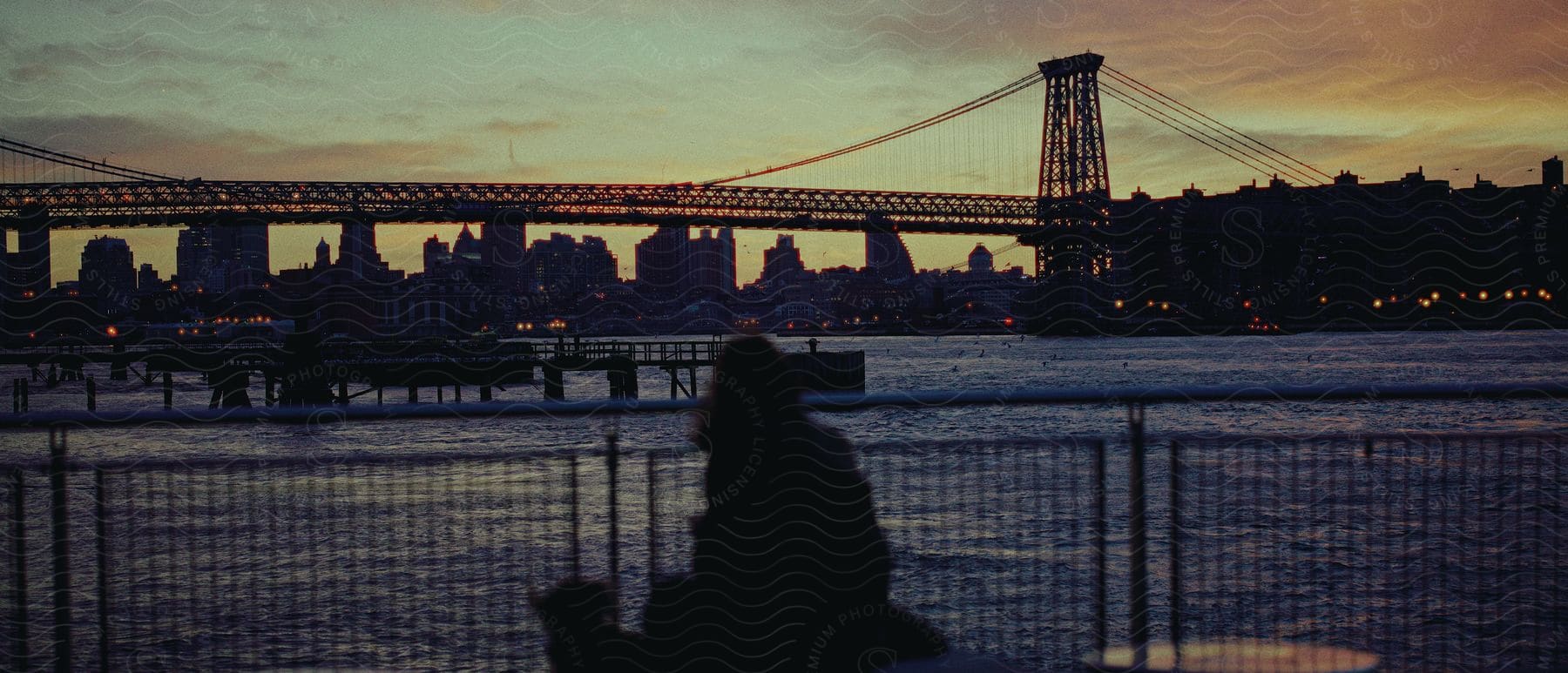 A city with a bridge over a body of water with a brown cloud in the evening