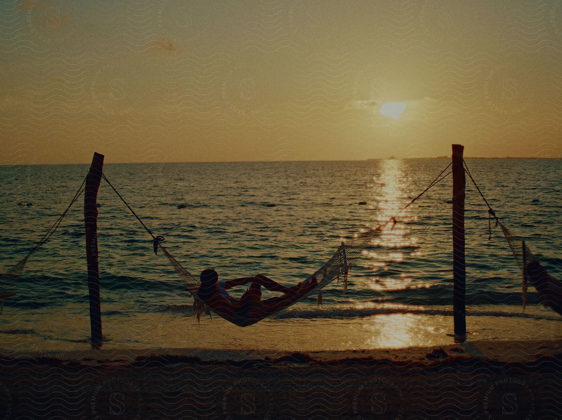 A person standing on a beach at dusk with a volleyball net in the background