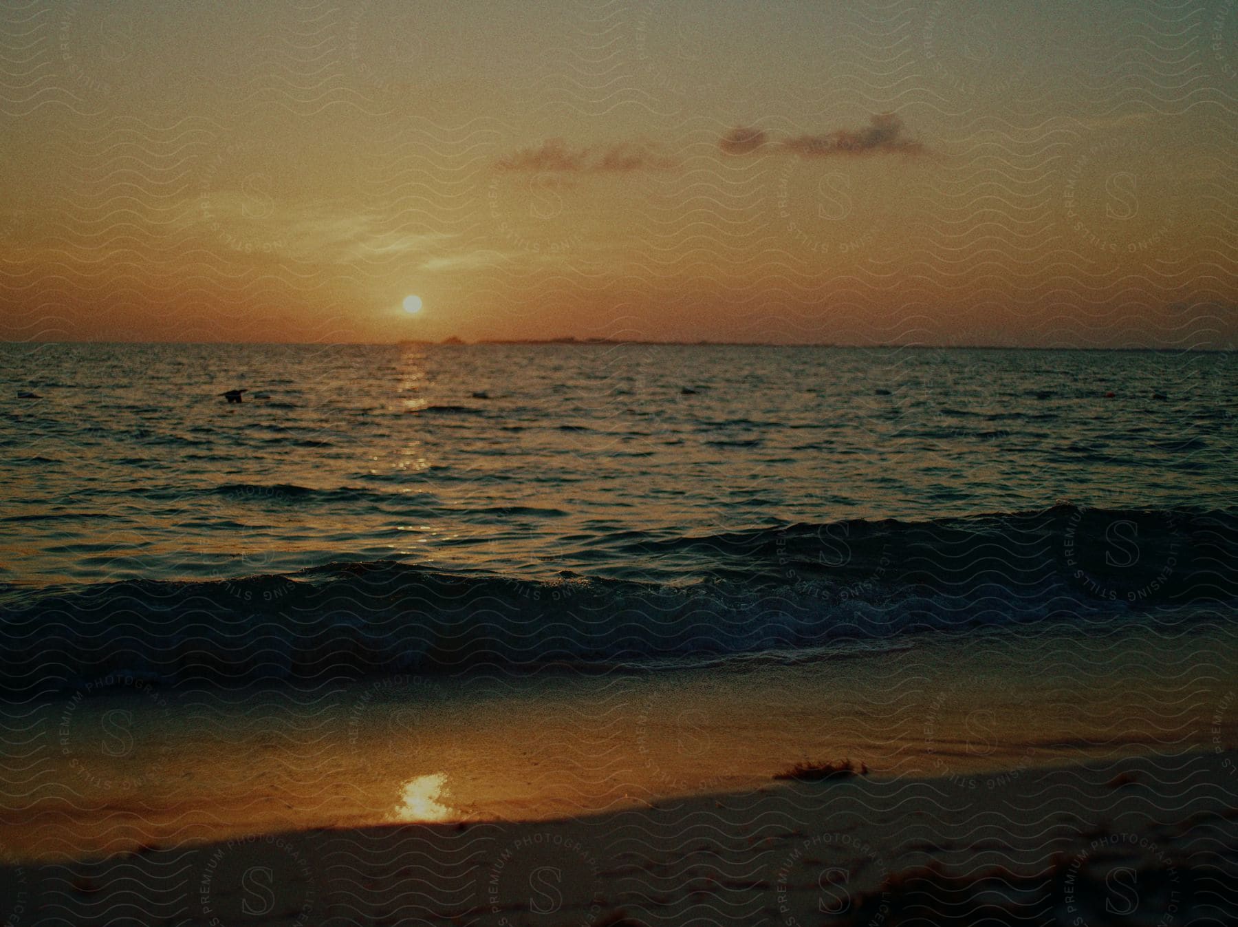 Waves roll over the beach as the setting sun reflects on the water in cancun